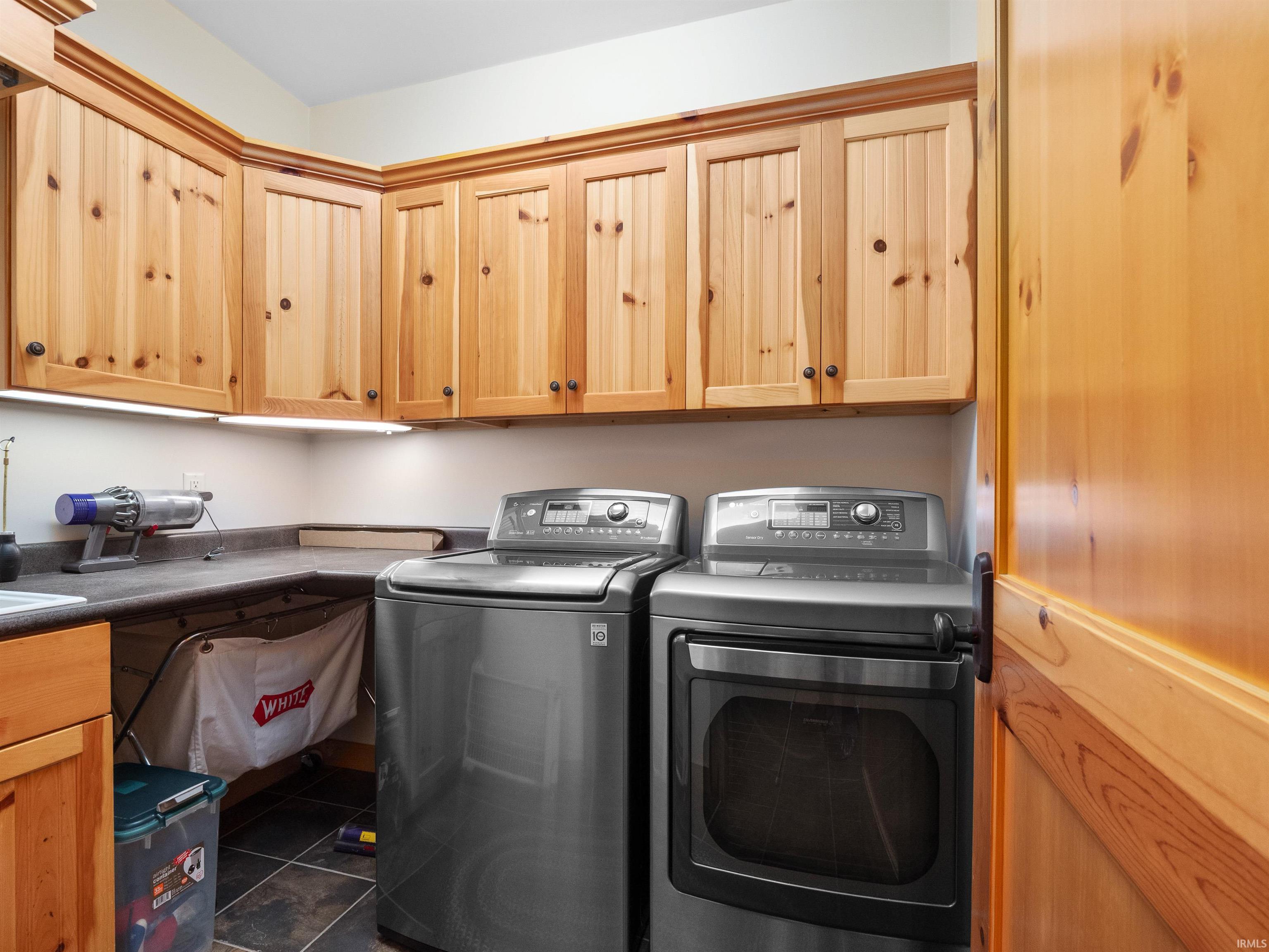 Laundry room featuring independent washer and dryer, cabinet space, and dark tile patterned floors