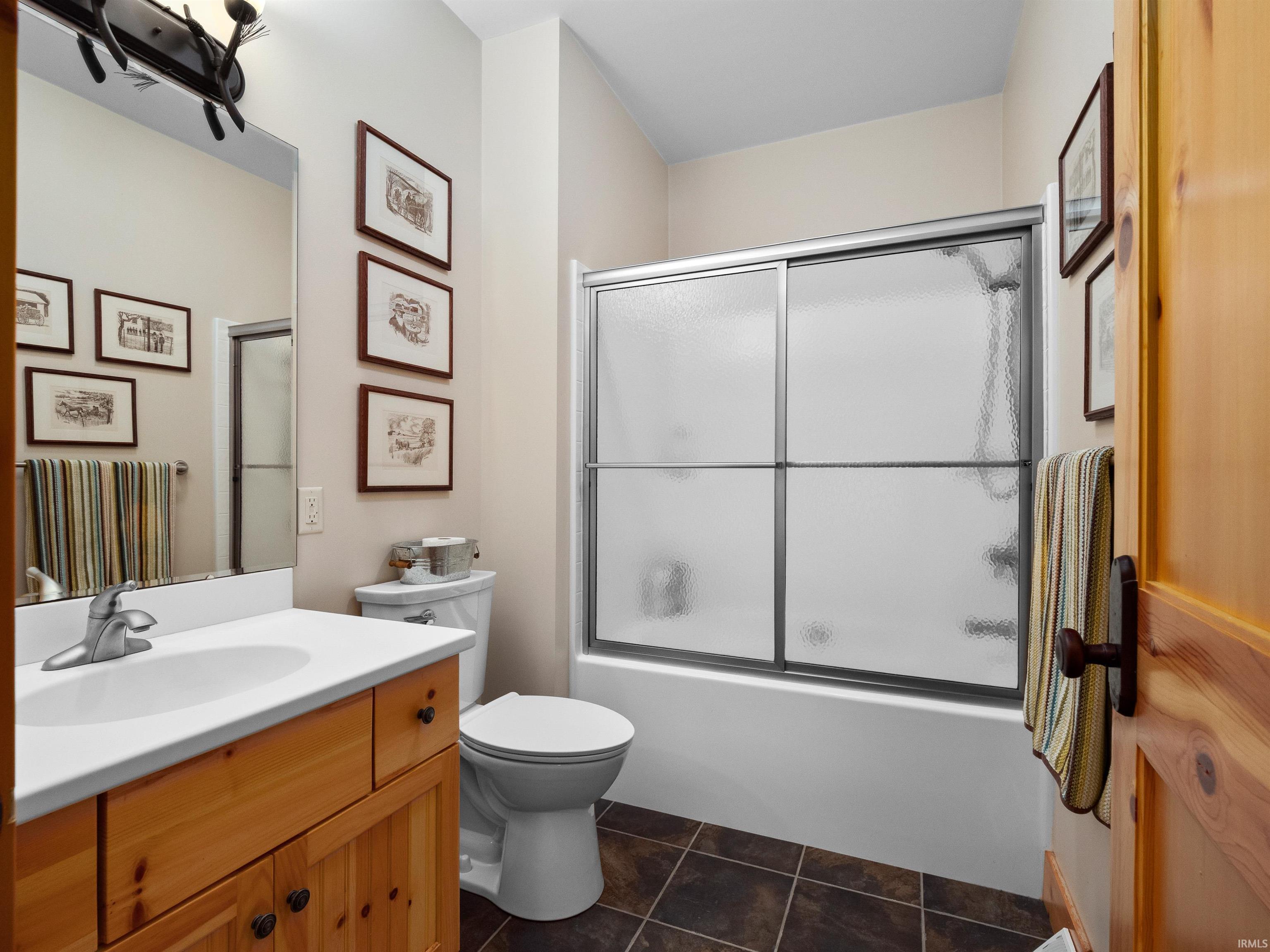 Full bath featuring vanity, enclosed tub / shower combo, and dark tile patterned floors