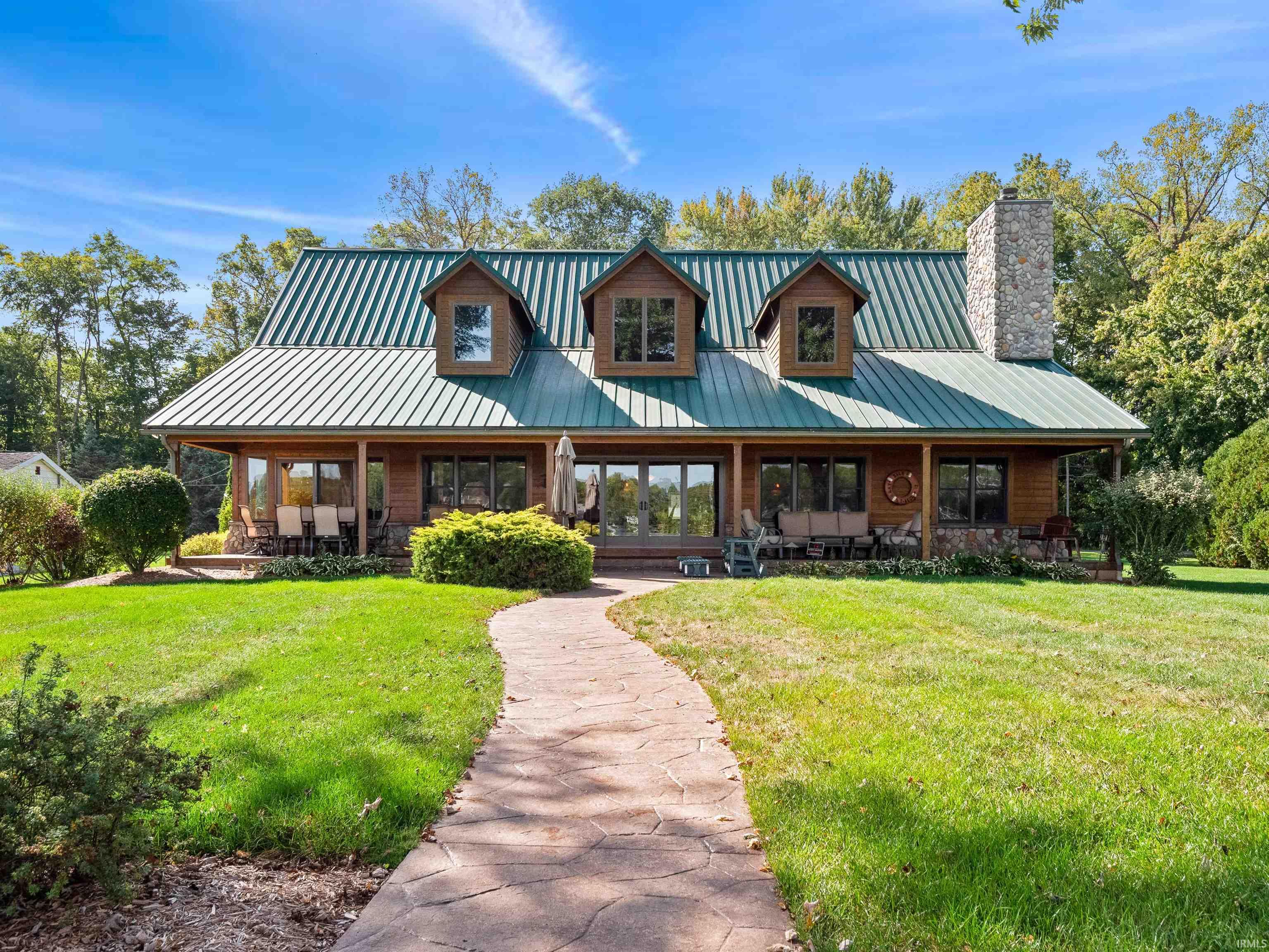 View of front facade featuring covered porch, a front lawn, a standing seam roof, and a chimney