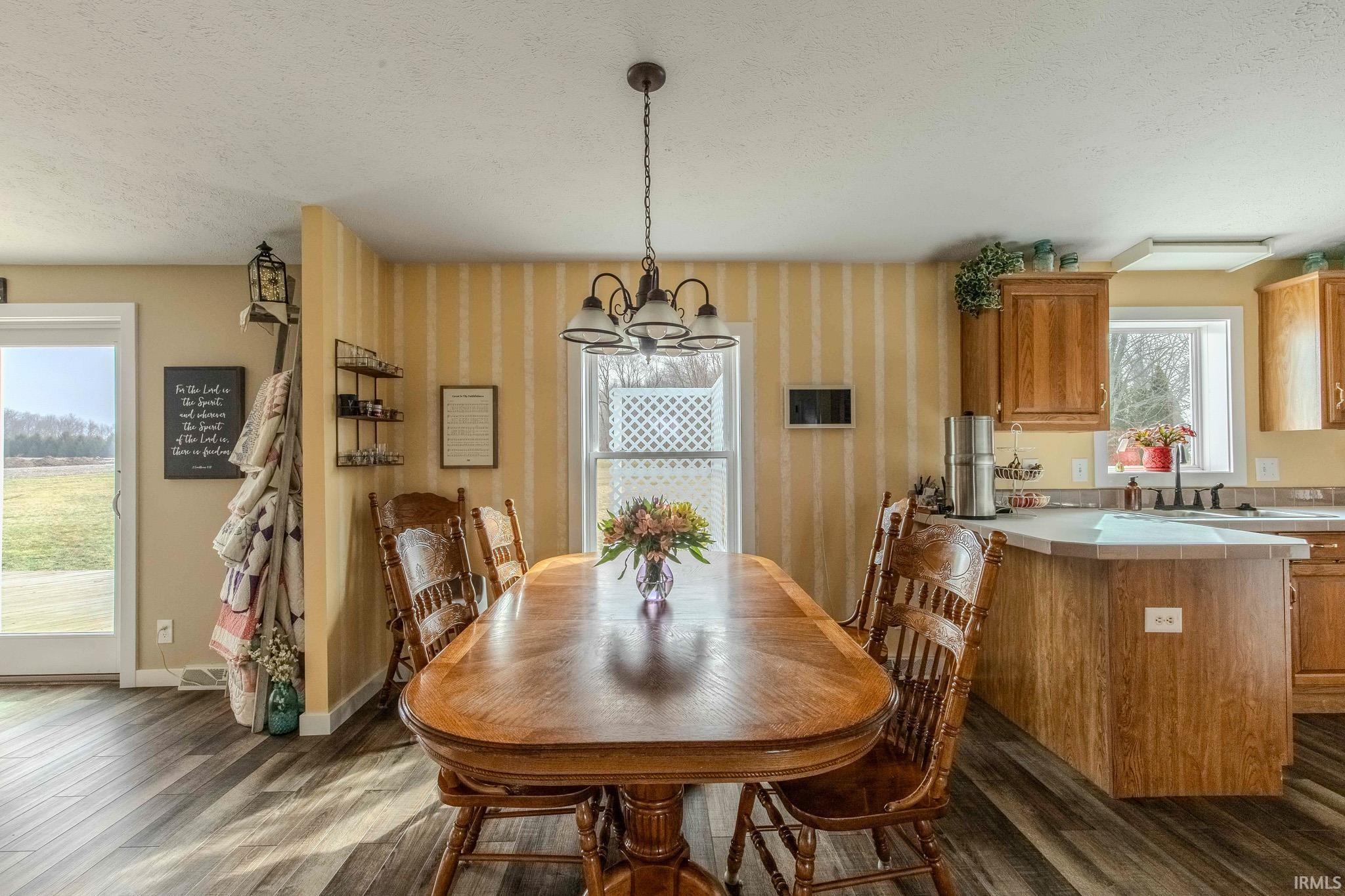 Dining area featuring a textured ceiling, hanging lights, dark wood-style flooring, and wallpapered walls