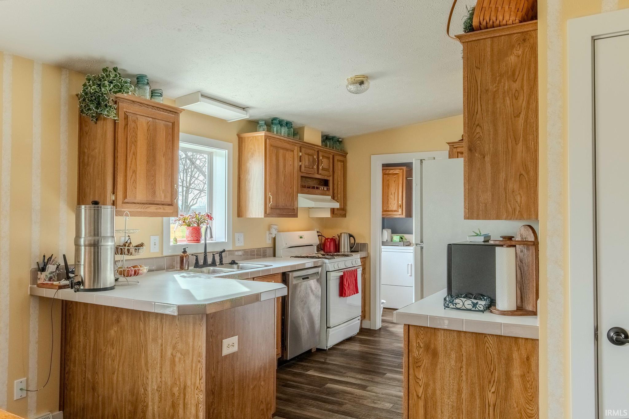 Kitchen with gas range gas stove, washer / clothes dryer, wood finish cabinetry, stainless steel dishwasher, and a peninsula