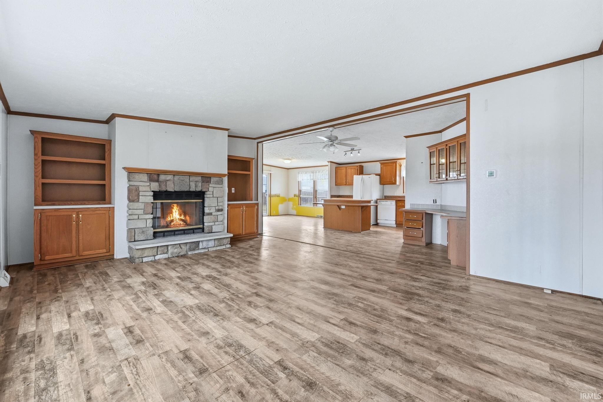 Unfurnished living room featuring ornamental molding, built in features, a fireplace, a ceiling fan, and light wood finished floors