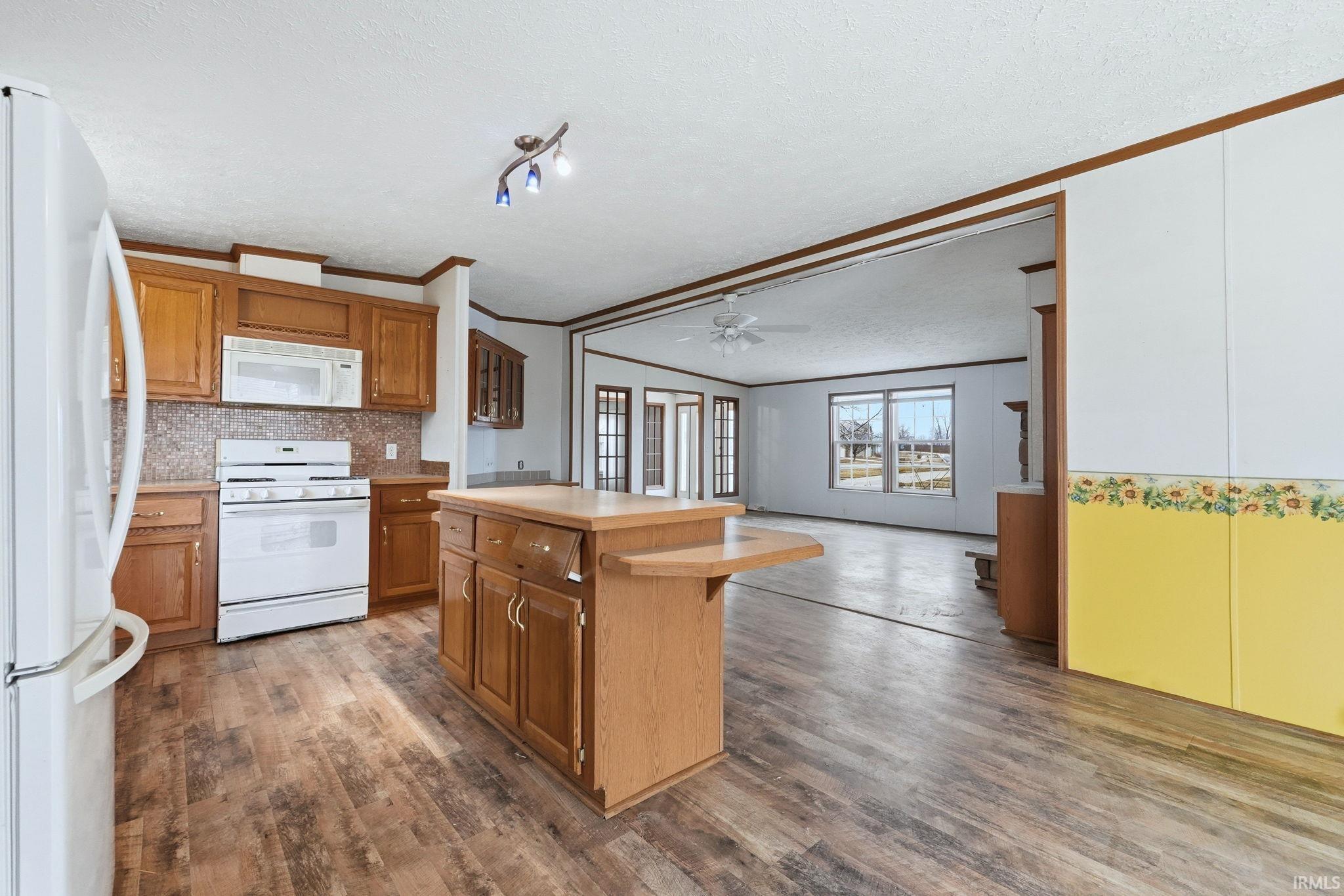 Kitchen featuring a kitchen bar, light countertops, white appliances, a textured ceiling, and open floor plan