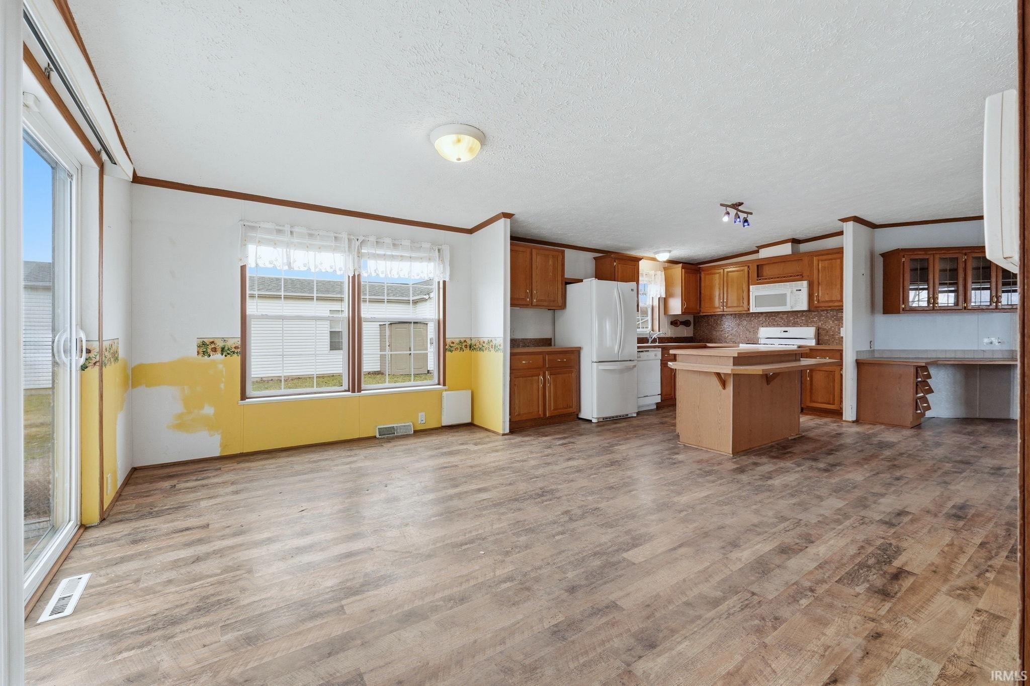 Kitchen with crown molding, wood finish cabinetry, white appliances, a kitchen island, and light wood-style floors