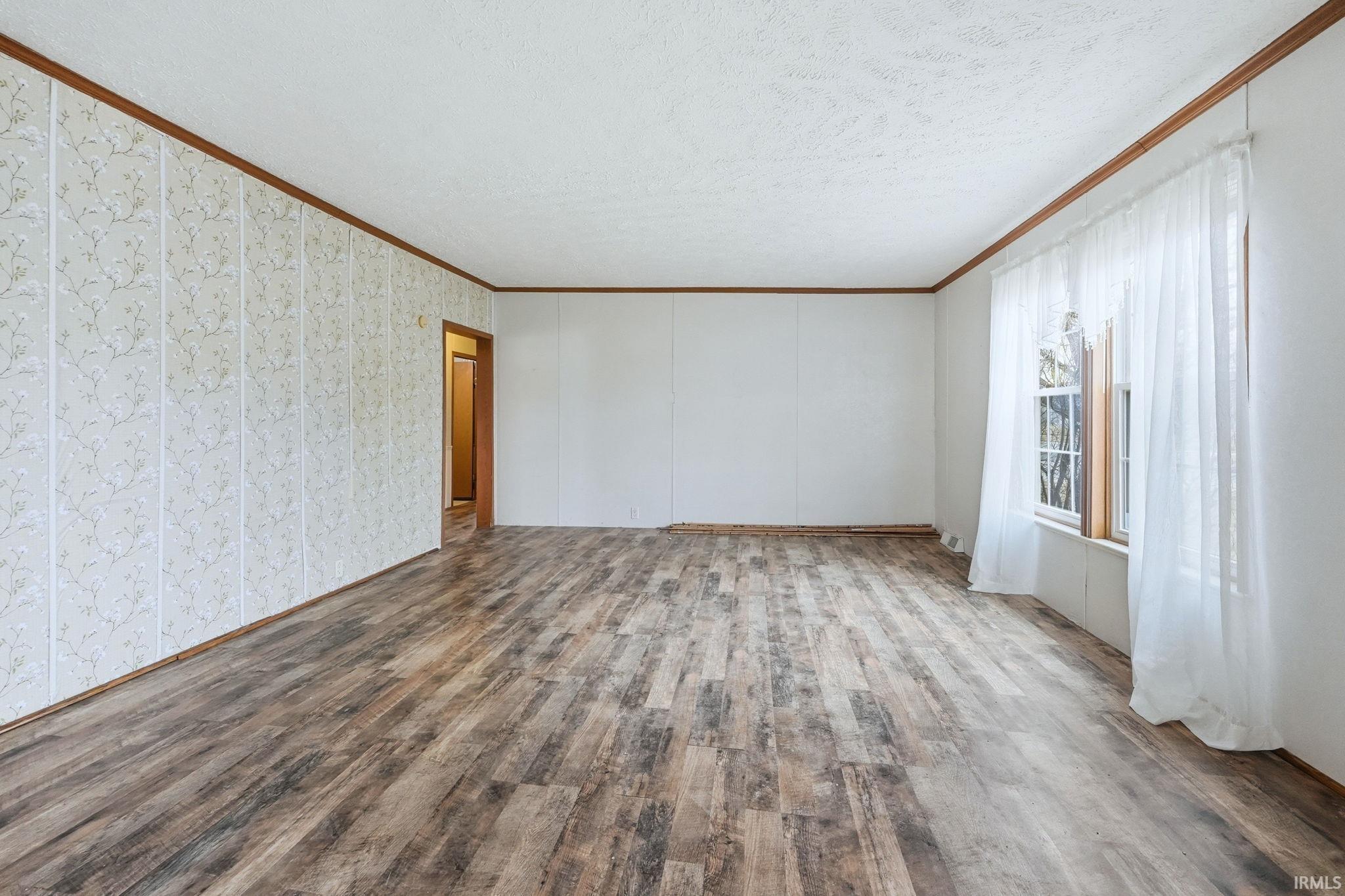 Empty room featuring ornamental molding, wood finished floors, and a textured ceiling