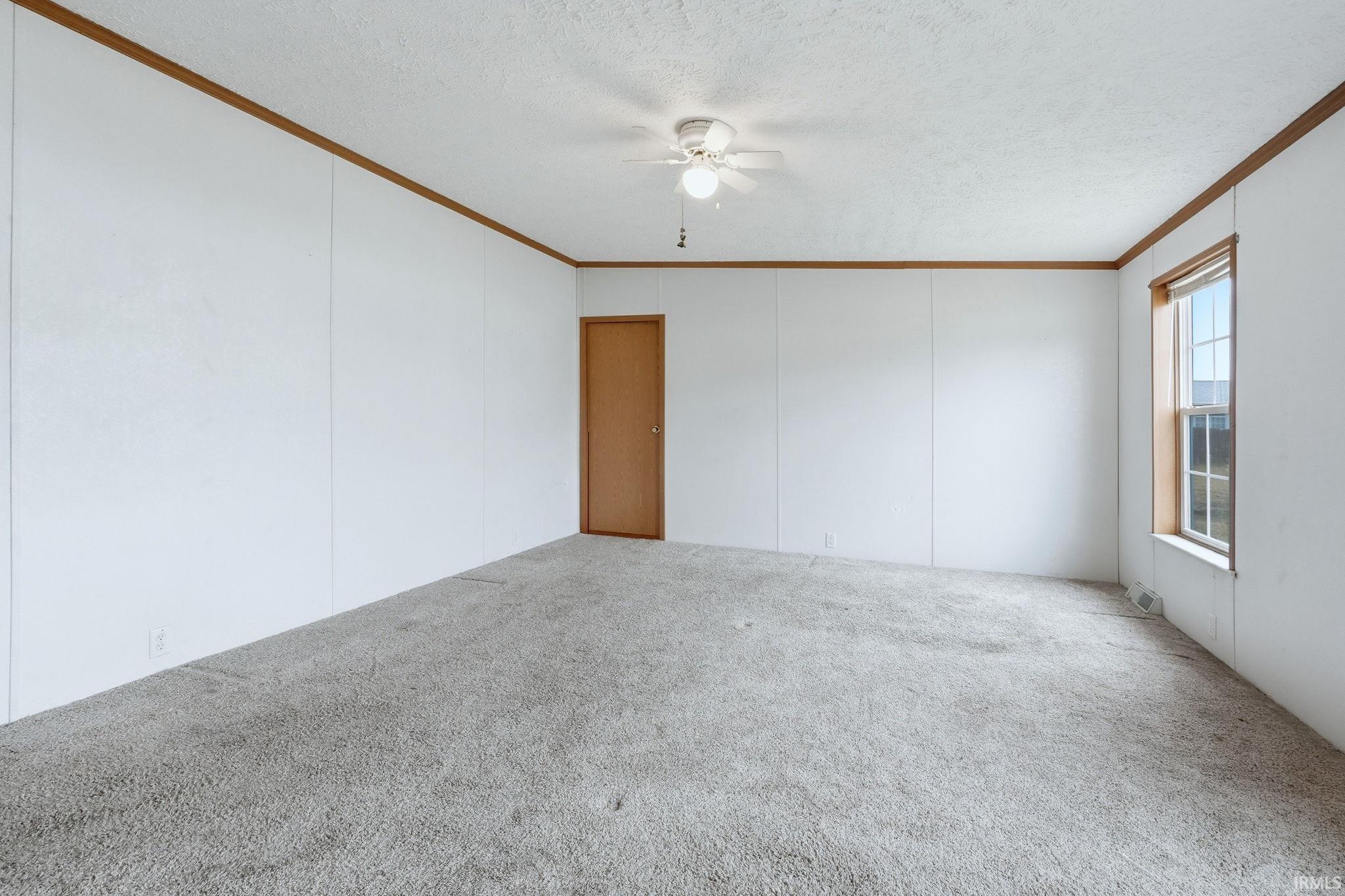 Unfurnished room with carpet flooring, a textured ceiling, crown molding, a ceiling fan, and a decorative wall