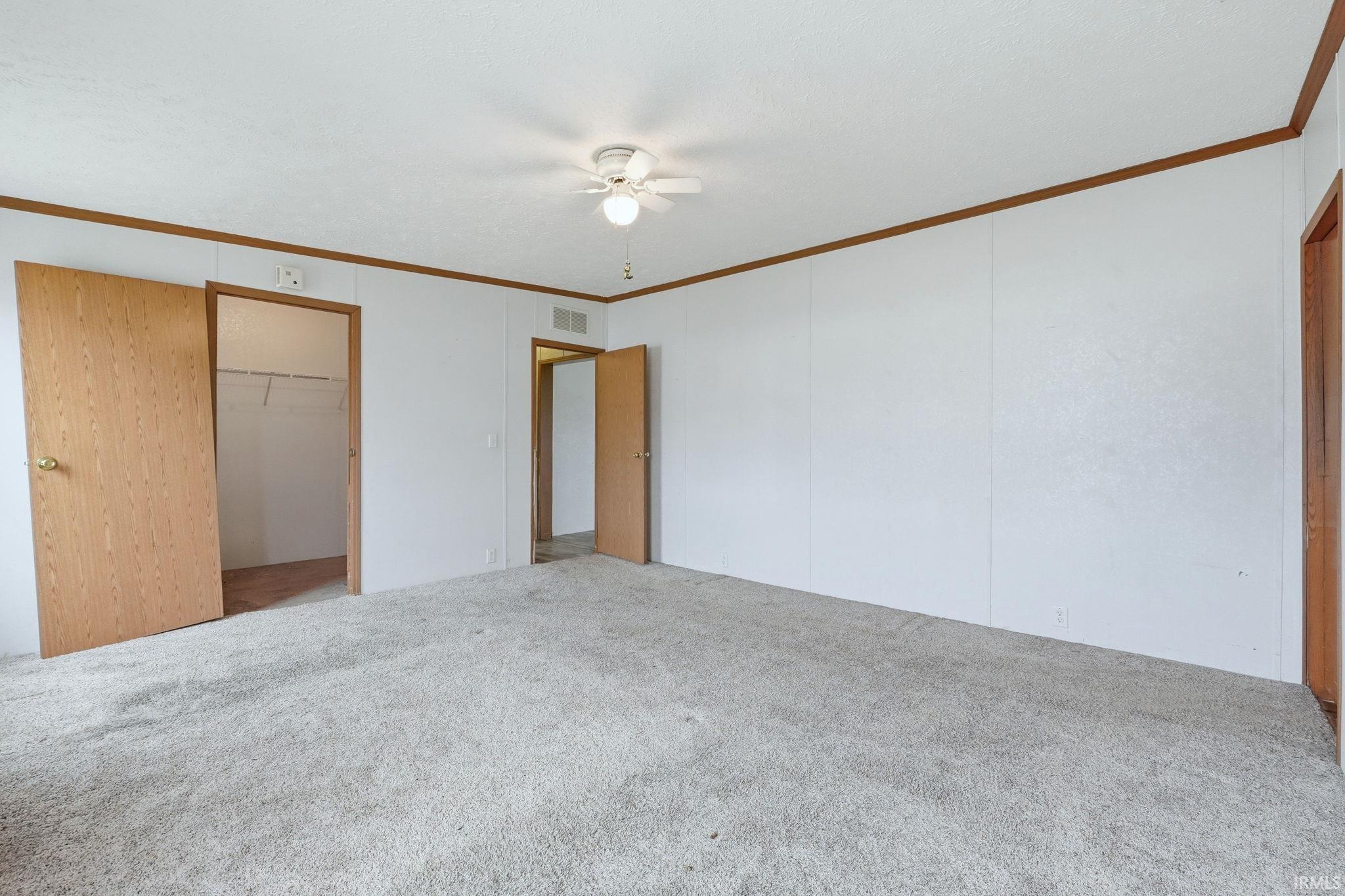 Unfurnished bedroom with light carpet, ornamental molding, a walk in closet, and ceiling fan