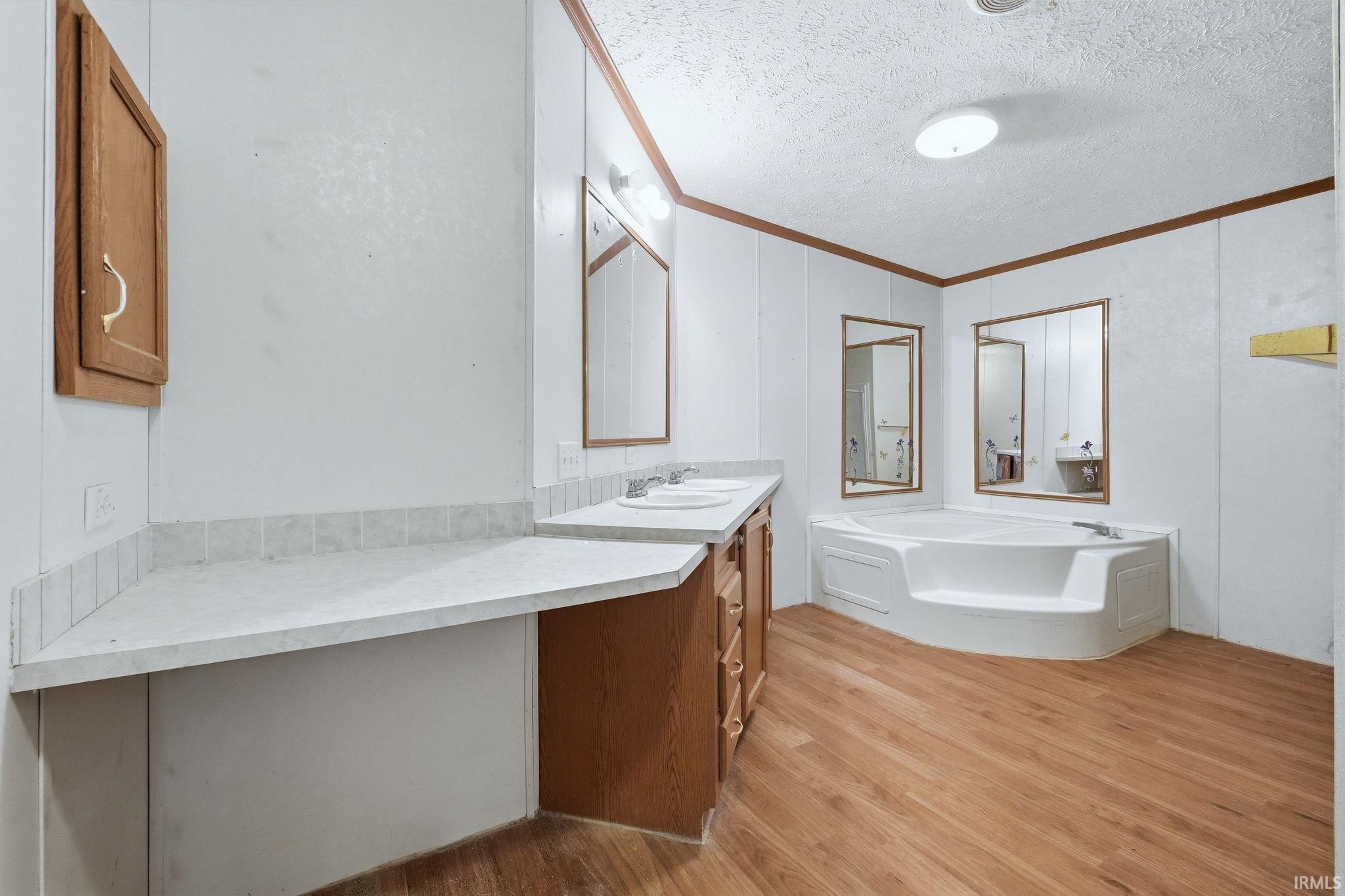 Full bath with vanity, light wood-type flooring, a textured ceiling, a garden tub, and ornamental molding