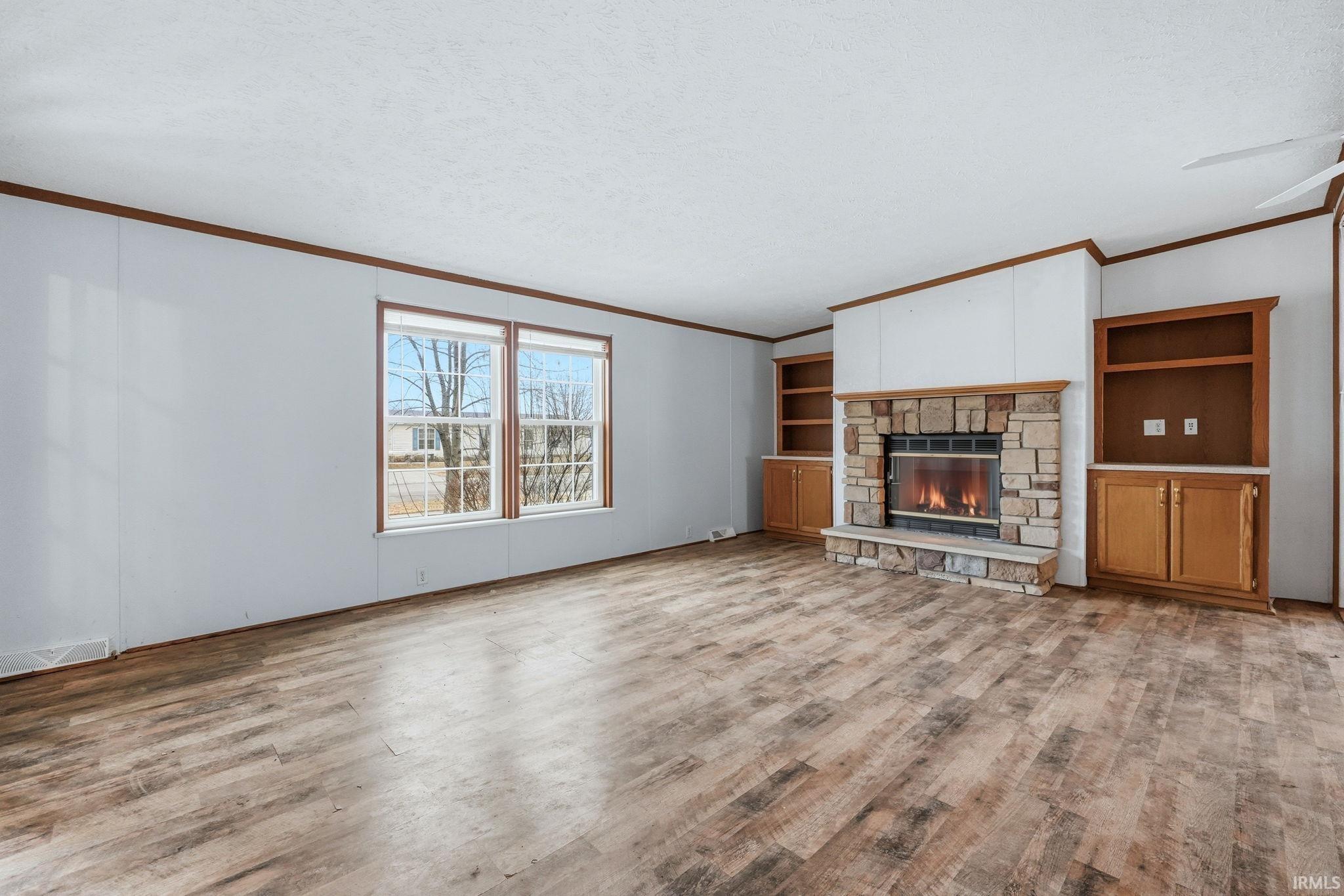 Unfurnished living room featuring light wood-style flooring, a fireplace, ornamental molding, a textured ceiling, and ceiling fan