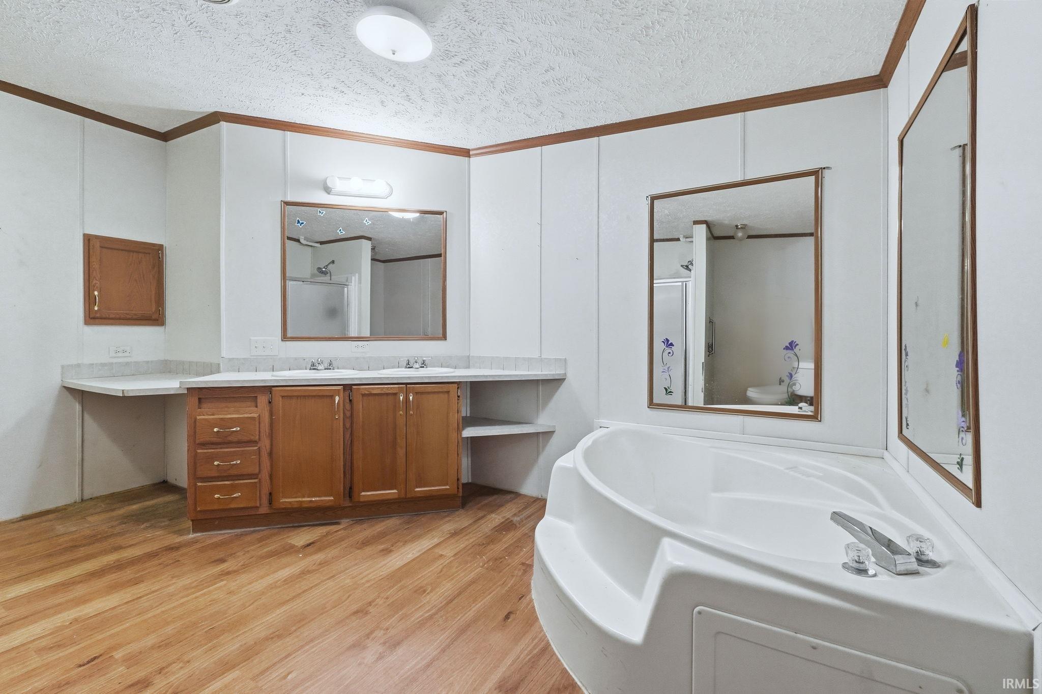 Bathroom with light wood-style floors, crown molding, vanity, a garden tub, and a textured ceiling