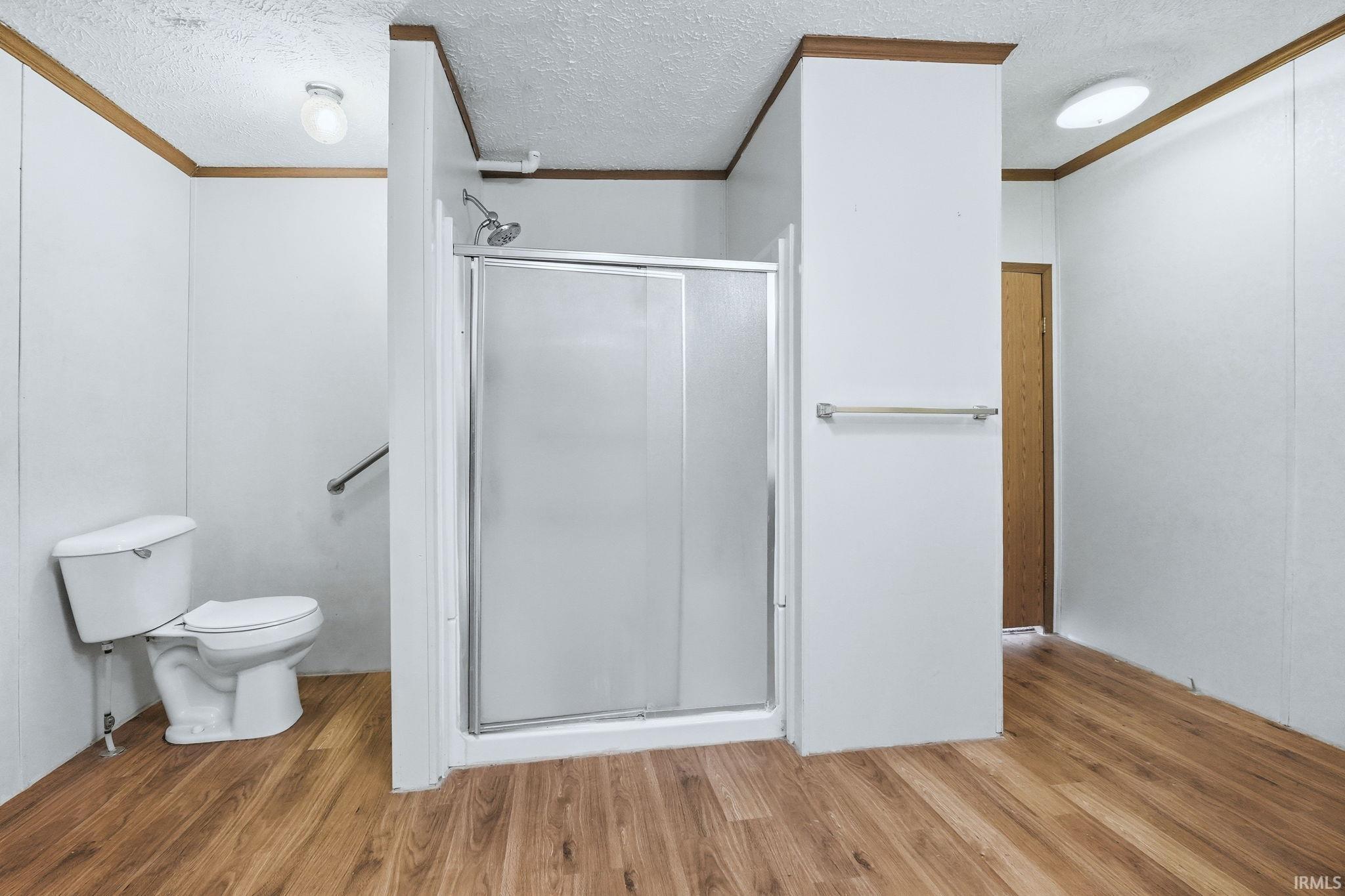 Bathroom with a shower stall, a textured ceiling, light wood finished floors, and ornamental molding