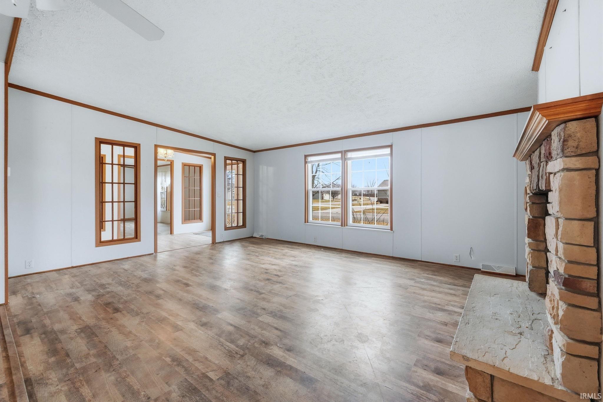 Unfurnished living room with light wood finished floors, a textured ceiling, ornamental molding, and ceiling fan
