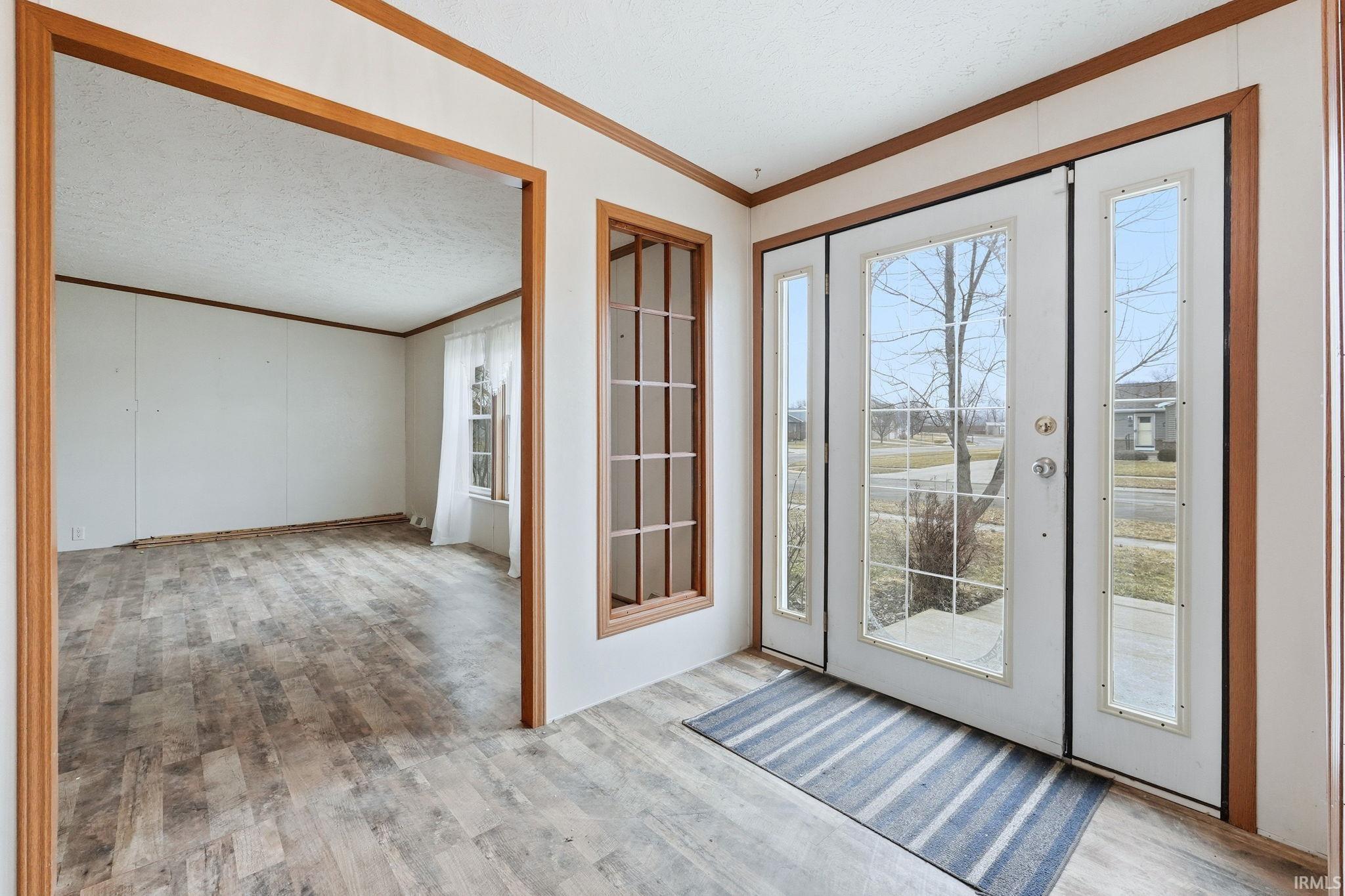 Entryway with crown molding, wood finished floors, and a textured ceiling