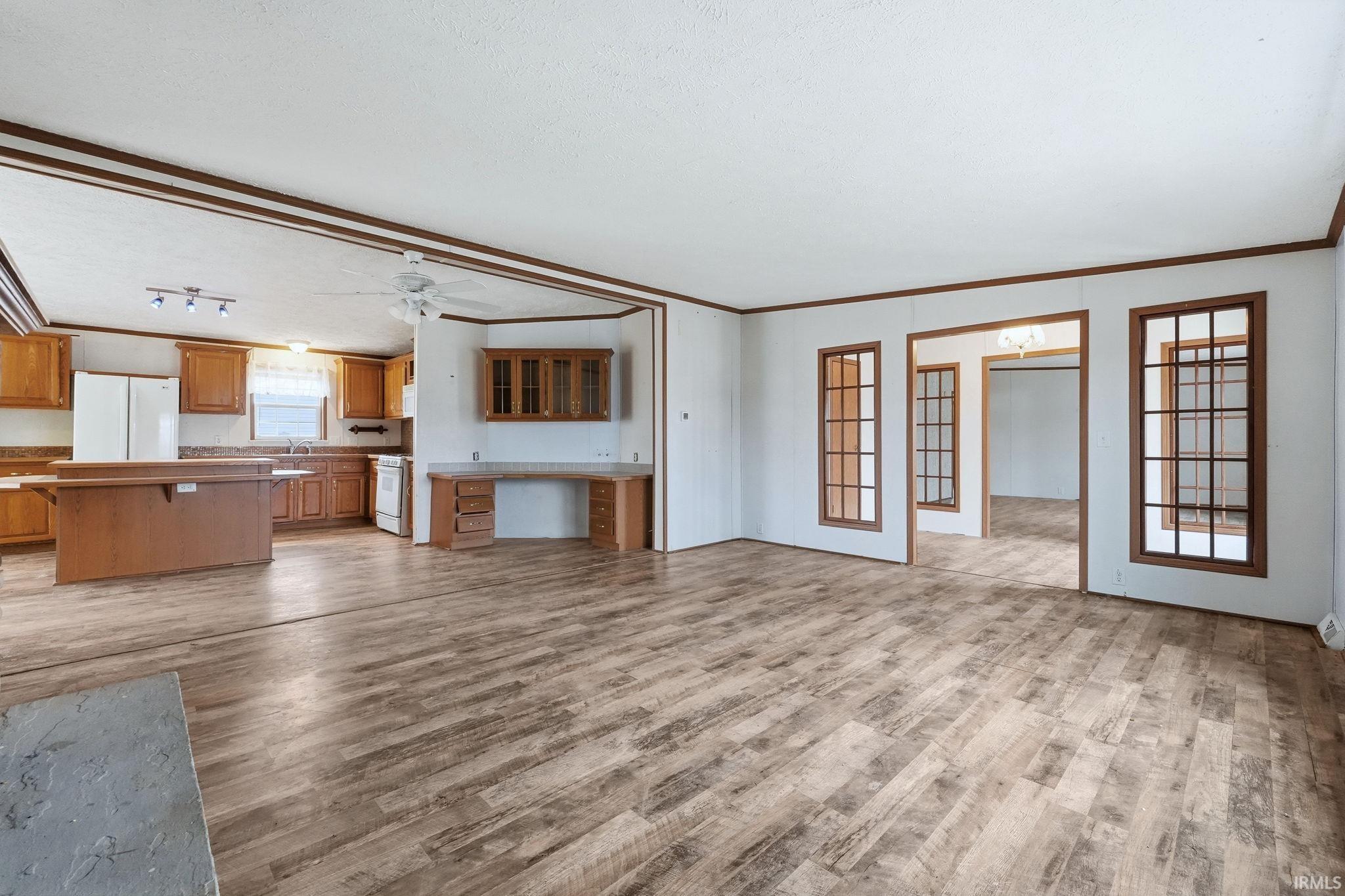 Unfurnished living room with light wood-style floors, a ceiling fan, and crown molding