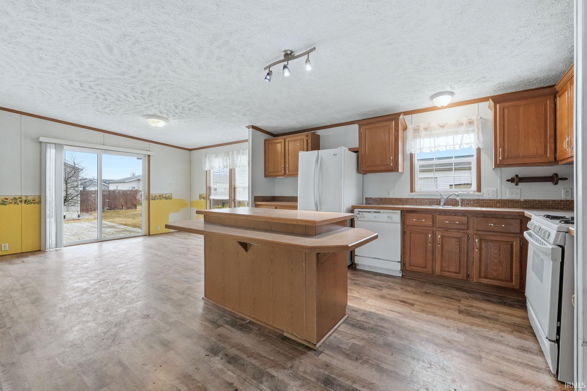 Kitchen featuring wood finish cabinetry, ornamental molding, a kitchen island, white appliances, and plenty of natural light