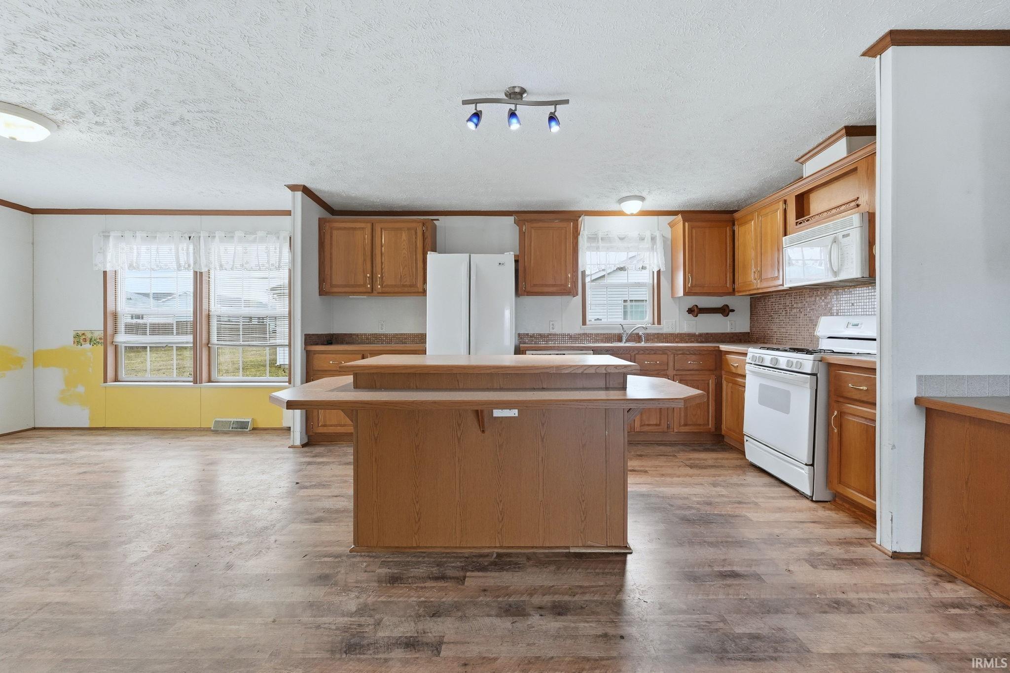 Kitchen featuring a kitchen bar, white appliances, a kitchen island, light countertops, and a textured ceiling