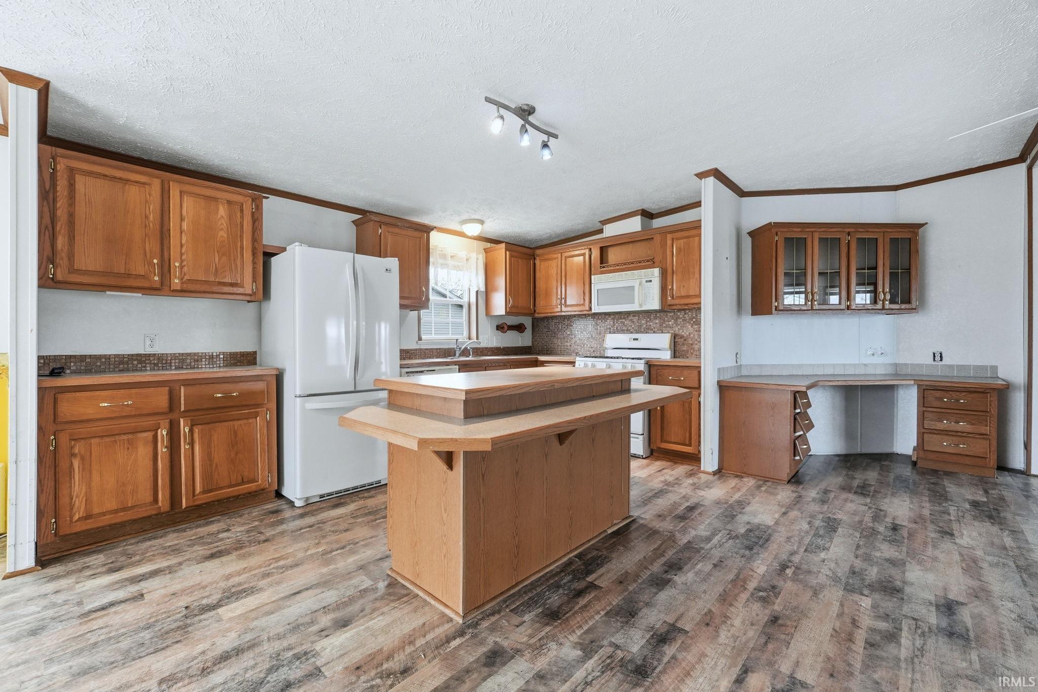Kitchen with a breakfast bar, a center island, white appliances, wood finish cabinetry, and crown molding