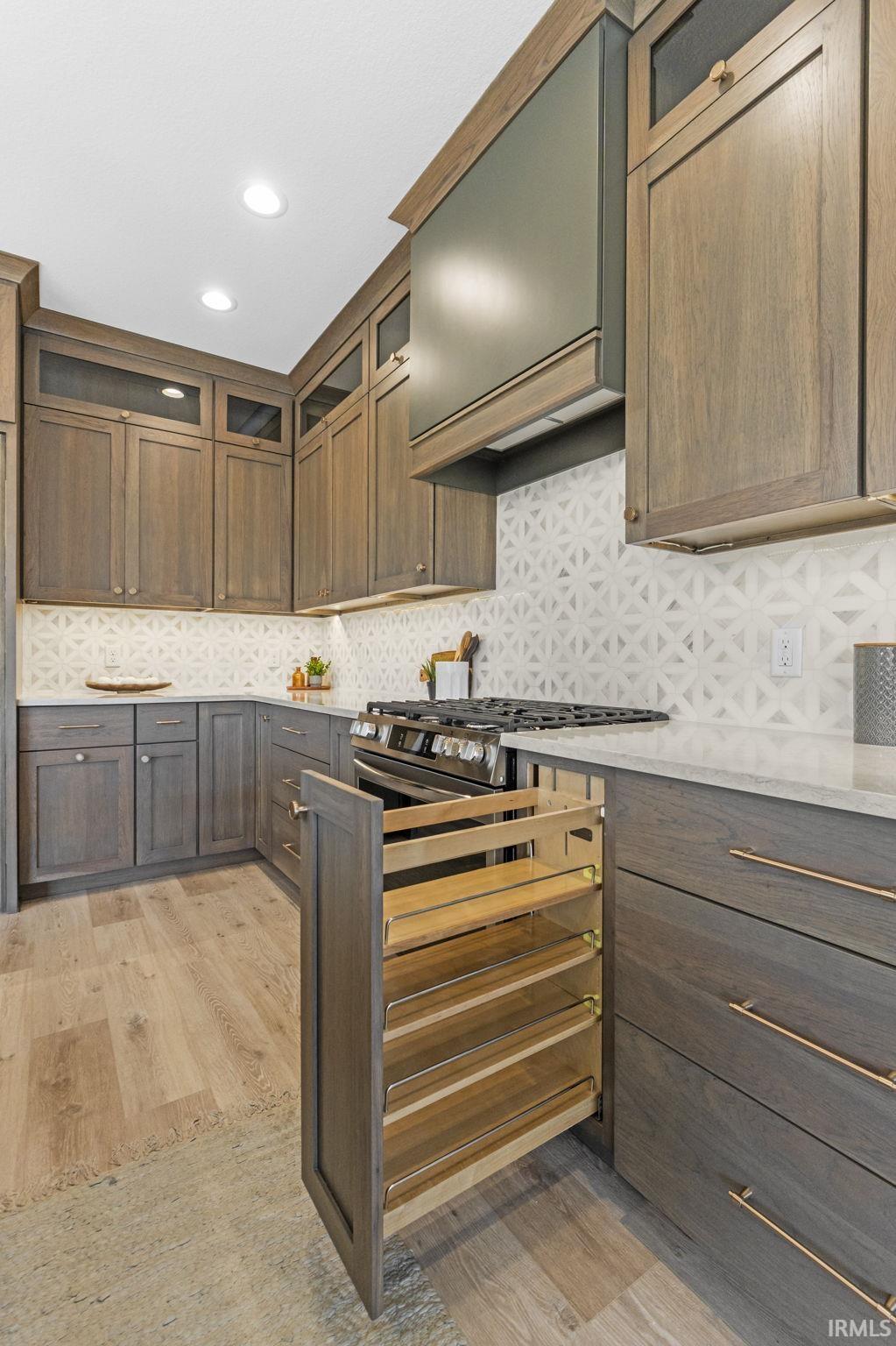 Kitchen with glass insert cabinets, light wood-style floors, custom range hood, recessed lighting, and light stone countertops