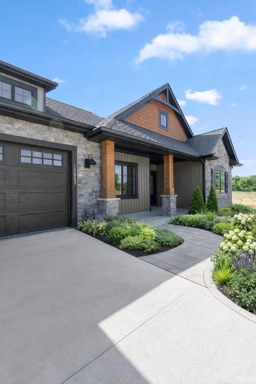 View of front of house with stone siding, board and batten siding, a garage, a porch, and driveway