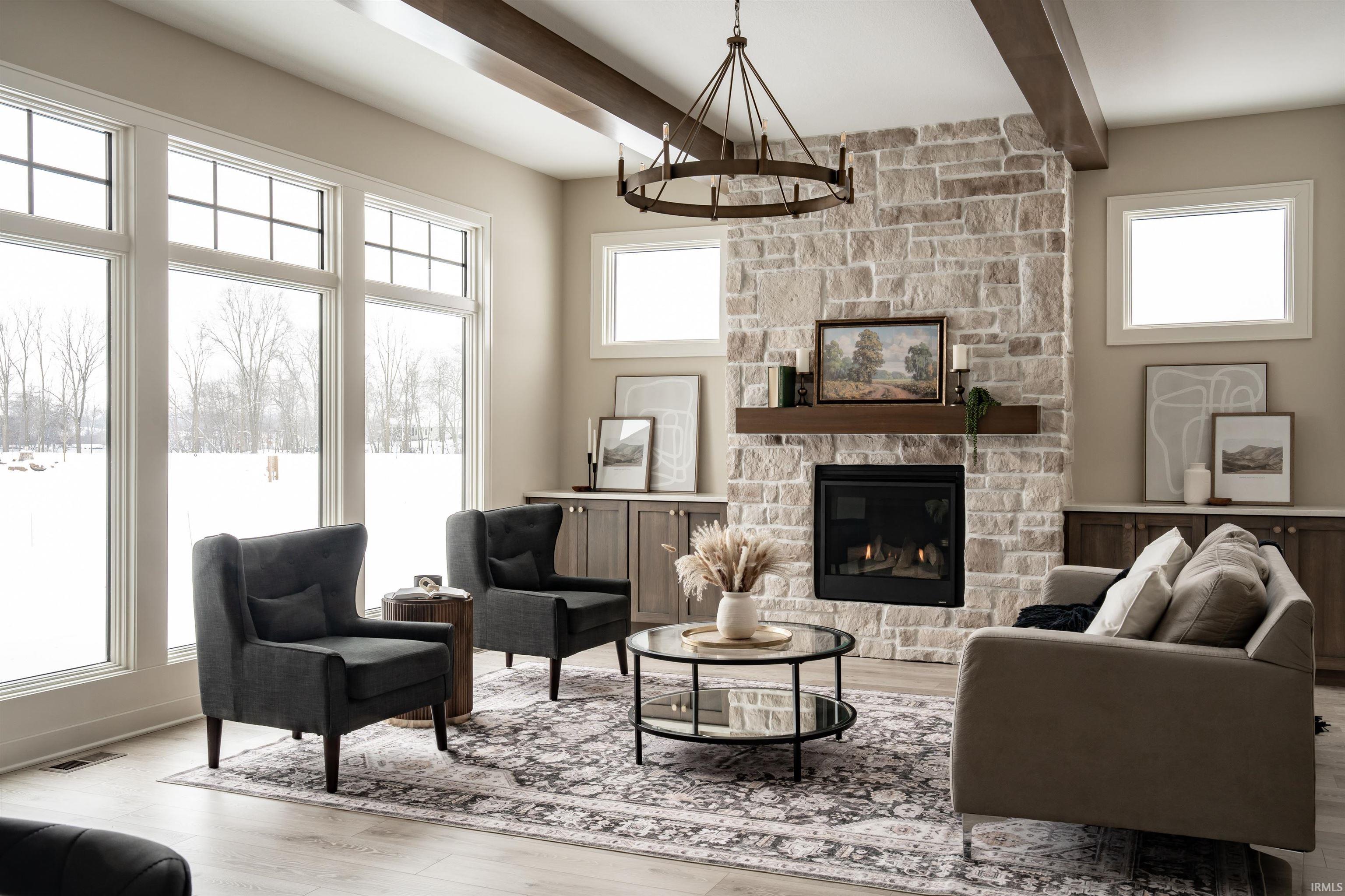 Living area with a stone fireplace, healthy amount of natural light, wood finished floors, and beam ceiling