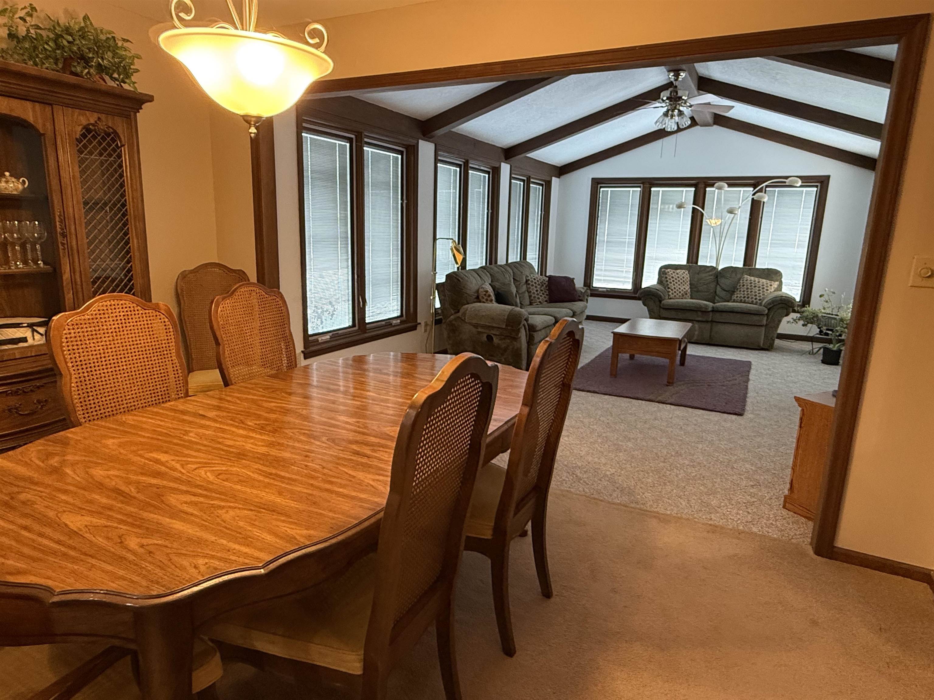 Dining area featuring light carpet, vaulted ceiling with beams, and a ceiling fan