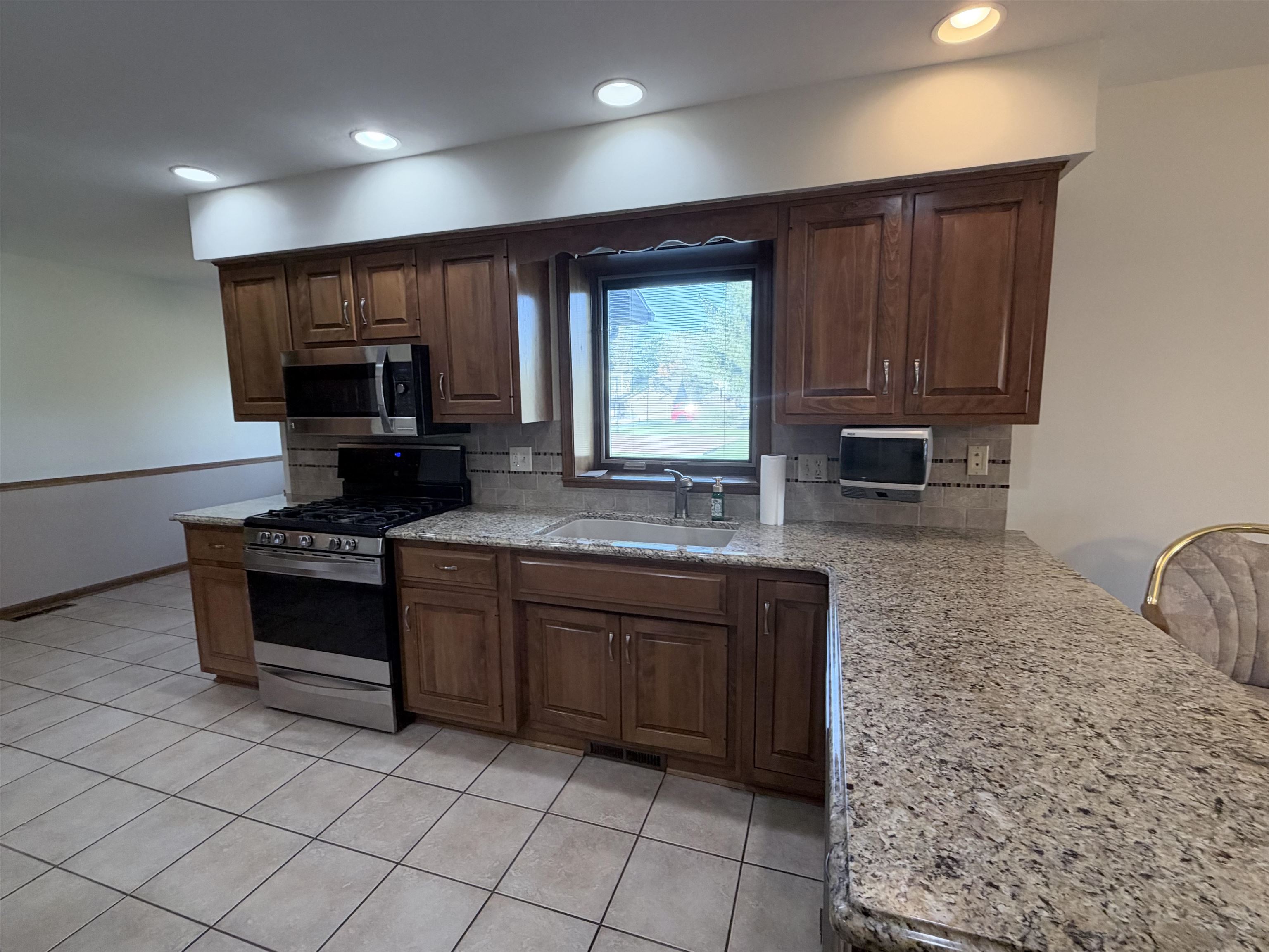 Kitchen featuring wood cabinetry, stone-surface countertops, tile flooring, recessed lighting, and stainless steel appliances