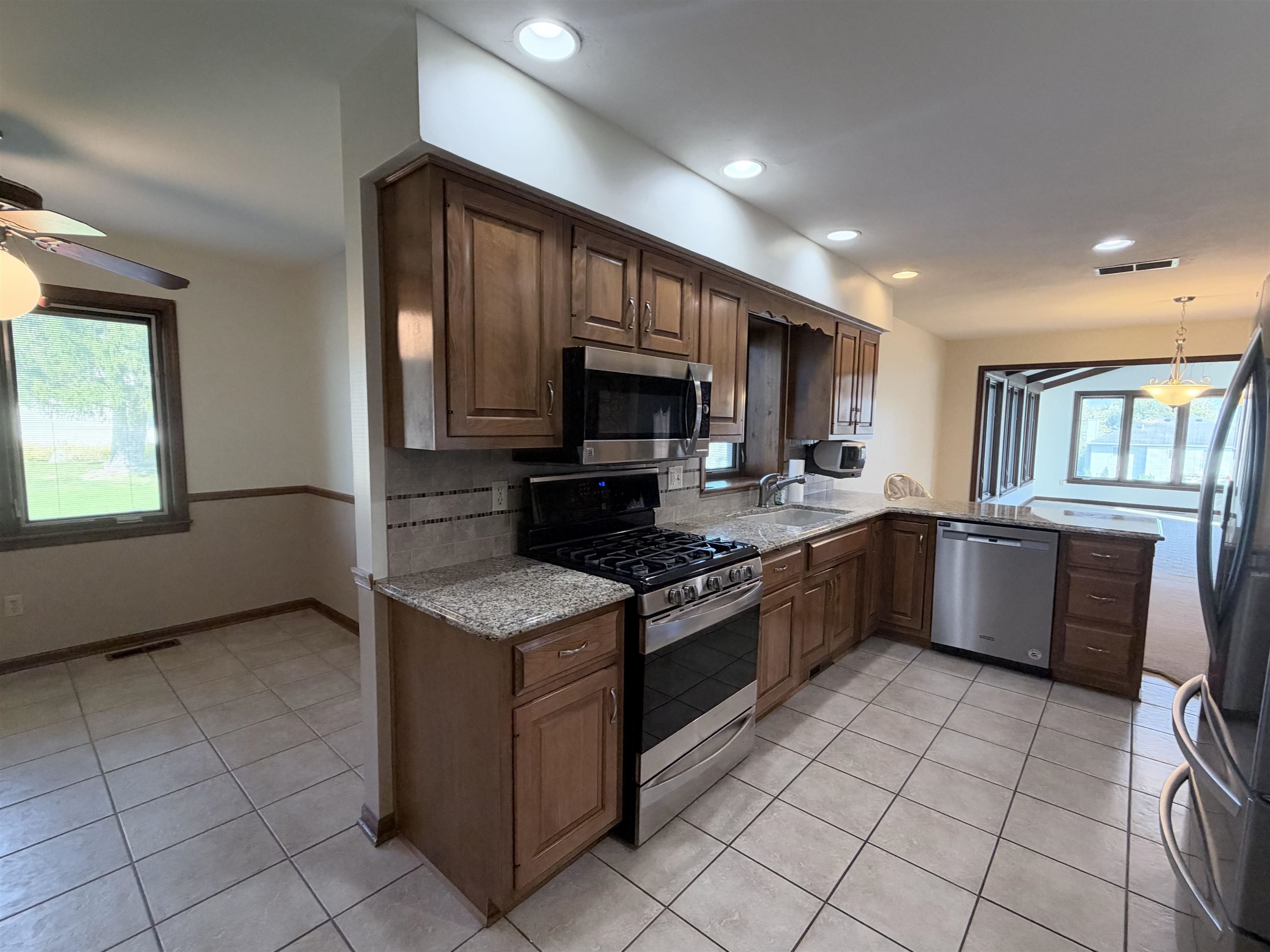 Kitchen featuring stained wood cabinetry, stone-finish countertops, stainless steel appliances, tile flooring, and recessed lighting
