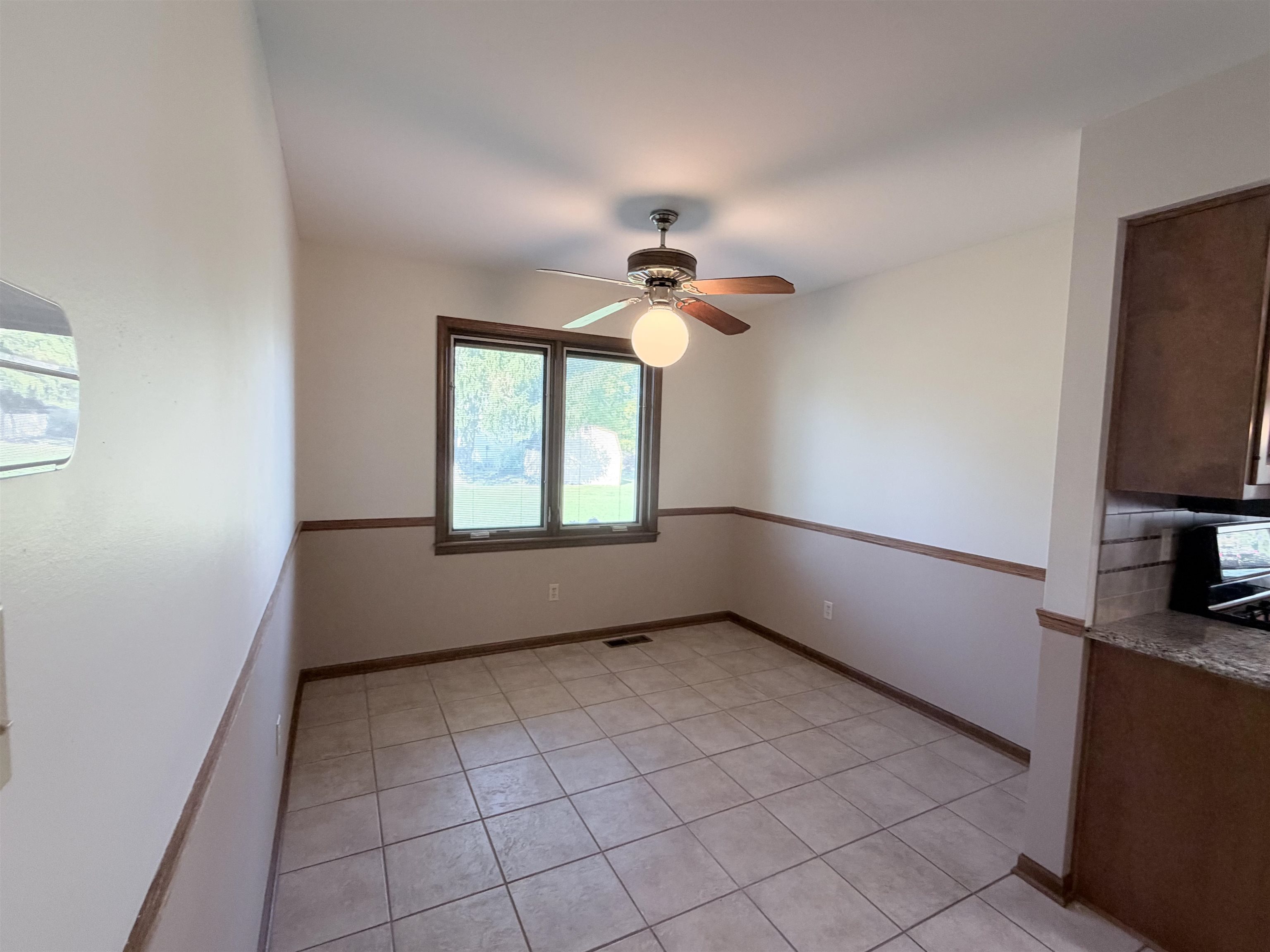 Ceramic tile flooring, neutral wall tones with wood chair rail molding, ceiling-mounted light fixture with fan, and window with natural illumination