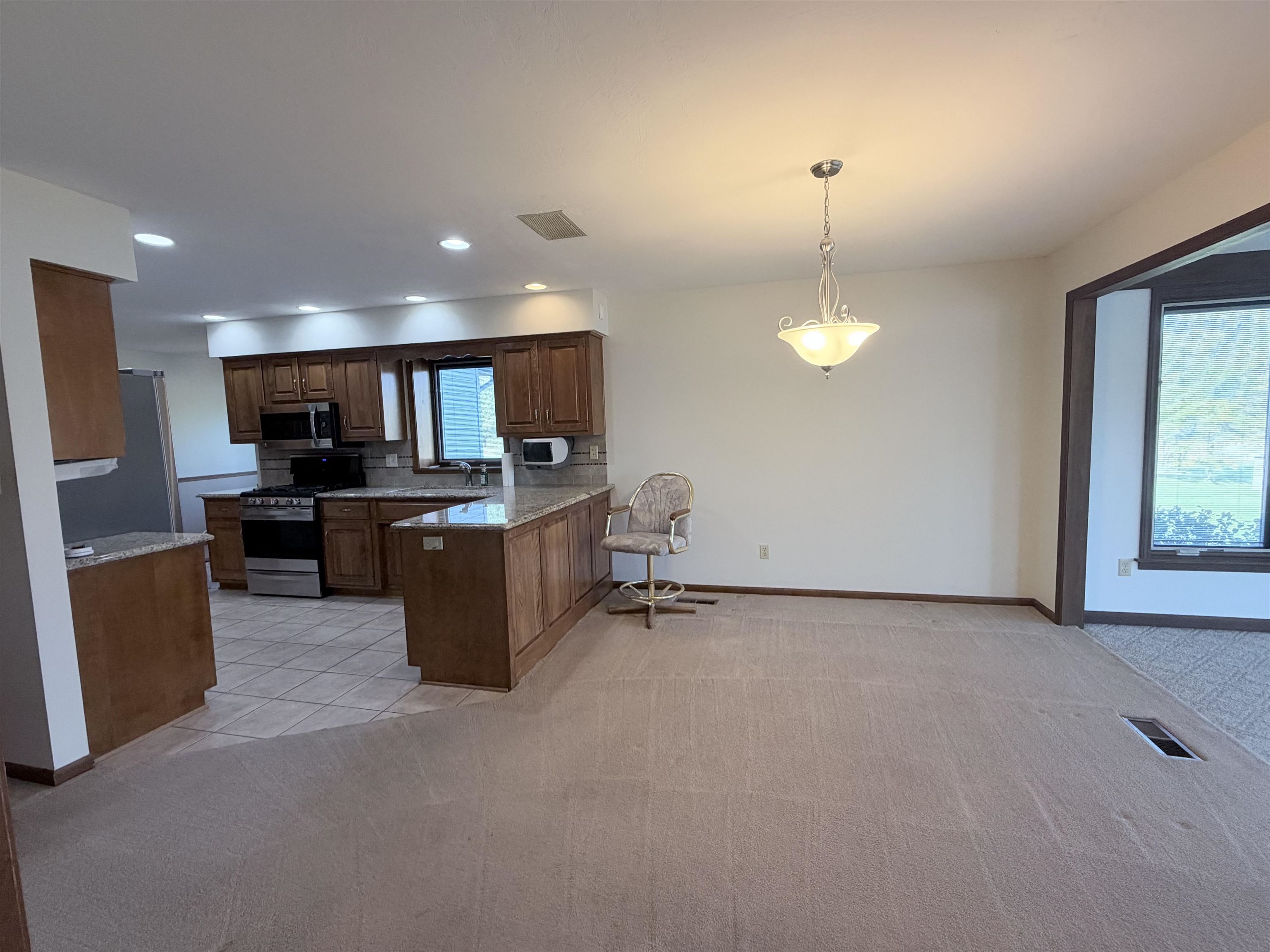 Kitchen featuring wood cabinetry, stone-finish countertops, stainless steel appliances, tiled flooring, and a decorative pendant light fixture