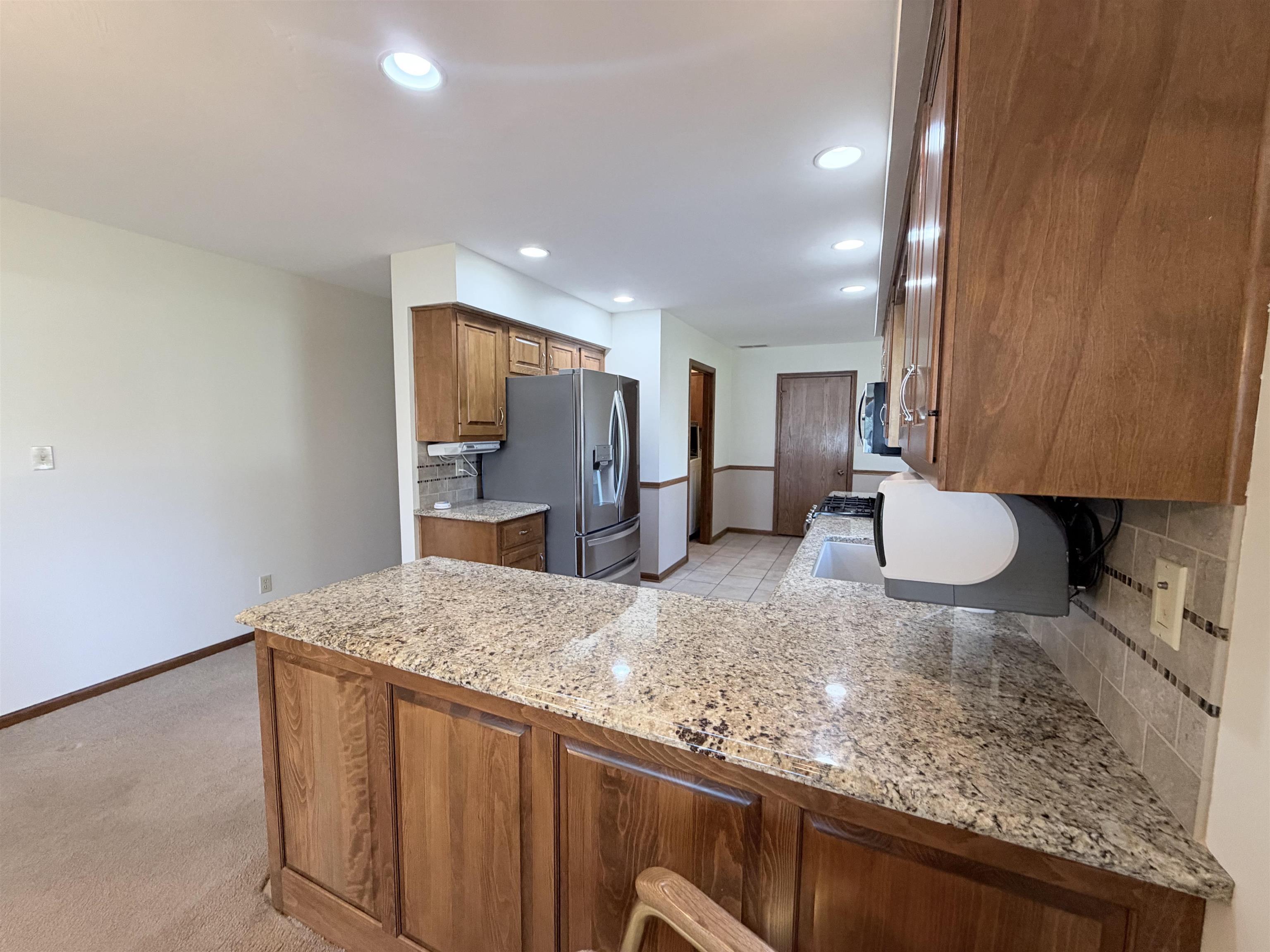 Kitchen featuring wood cabinetry, stone-surface breakfast bar, recessed lighting, and ceramic tile backsplash