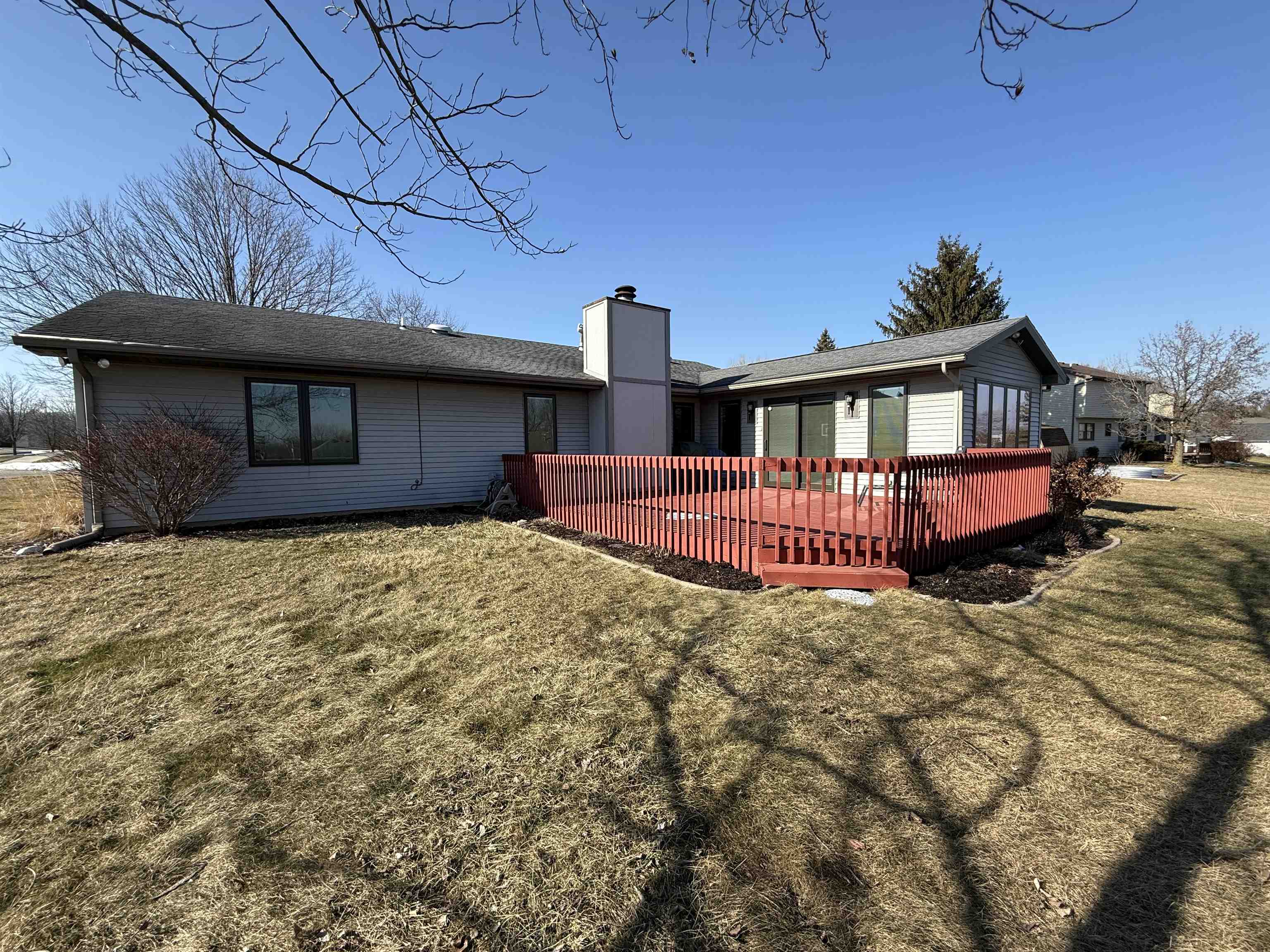Rear view of property with a lawn, a chimney, a wooden deck, and roof with shingles