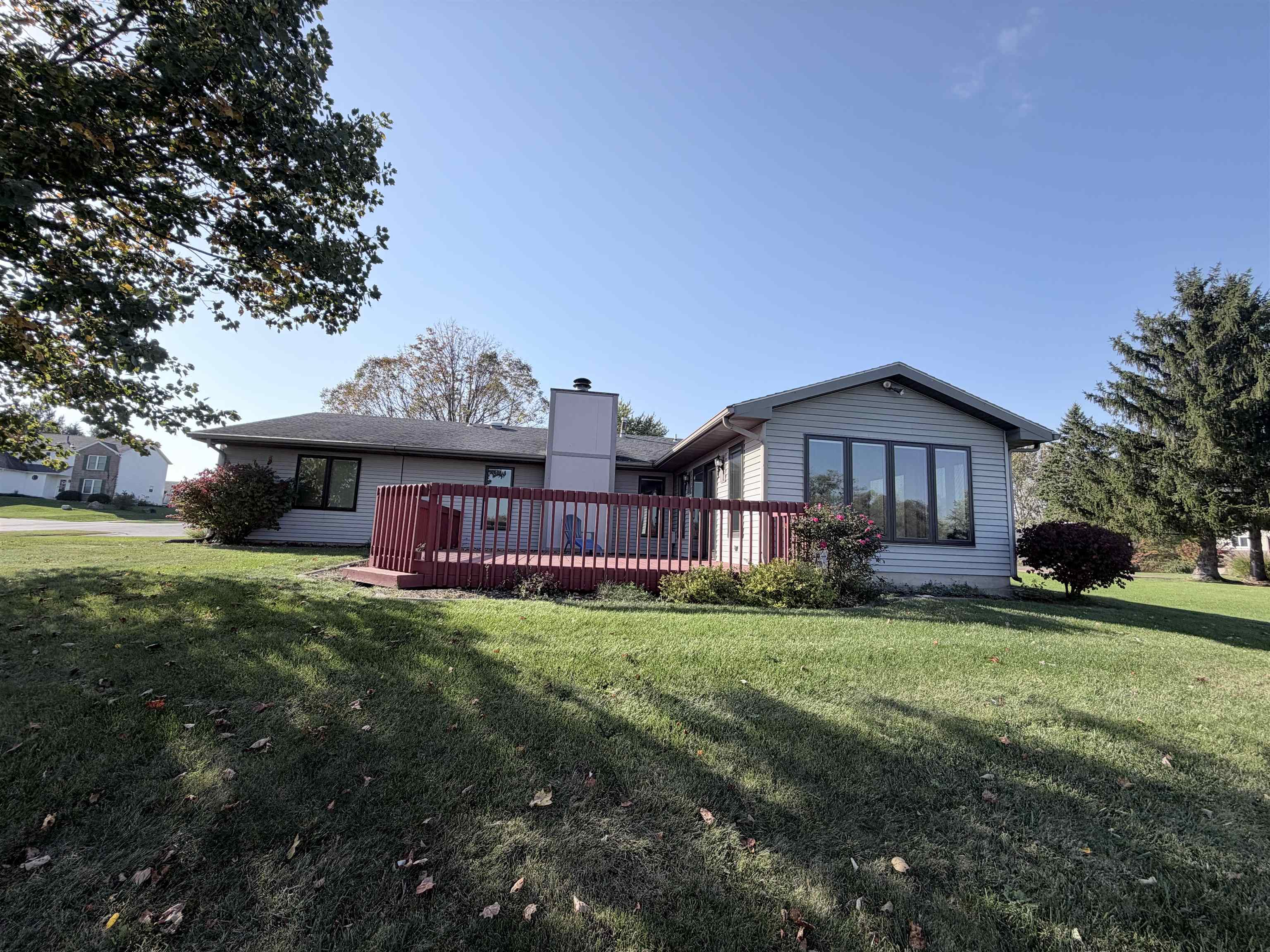 Exterior elevation featuring horizontal siding, a raised deck with perimeter railing, central chimney, and expansive lawn with mature trees