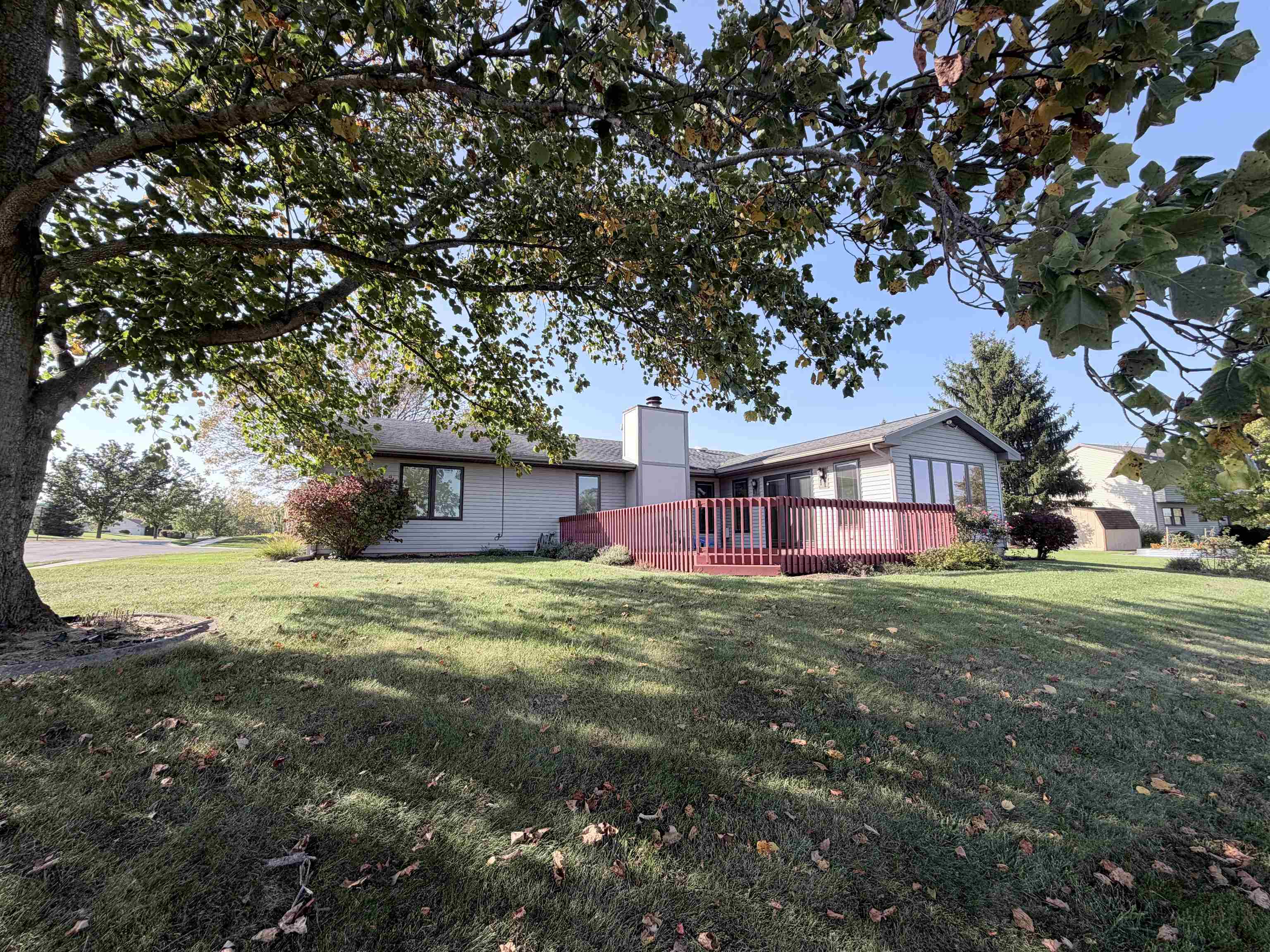 Expansive lawn featuring mature trees and a raised wooden deck with an exterior fireplace chimney