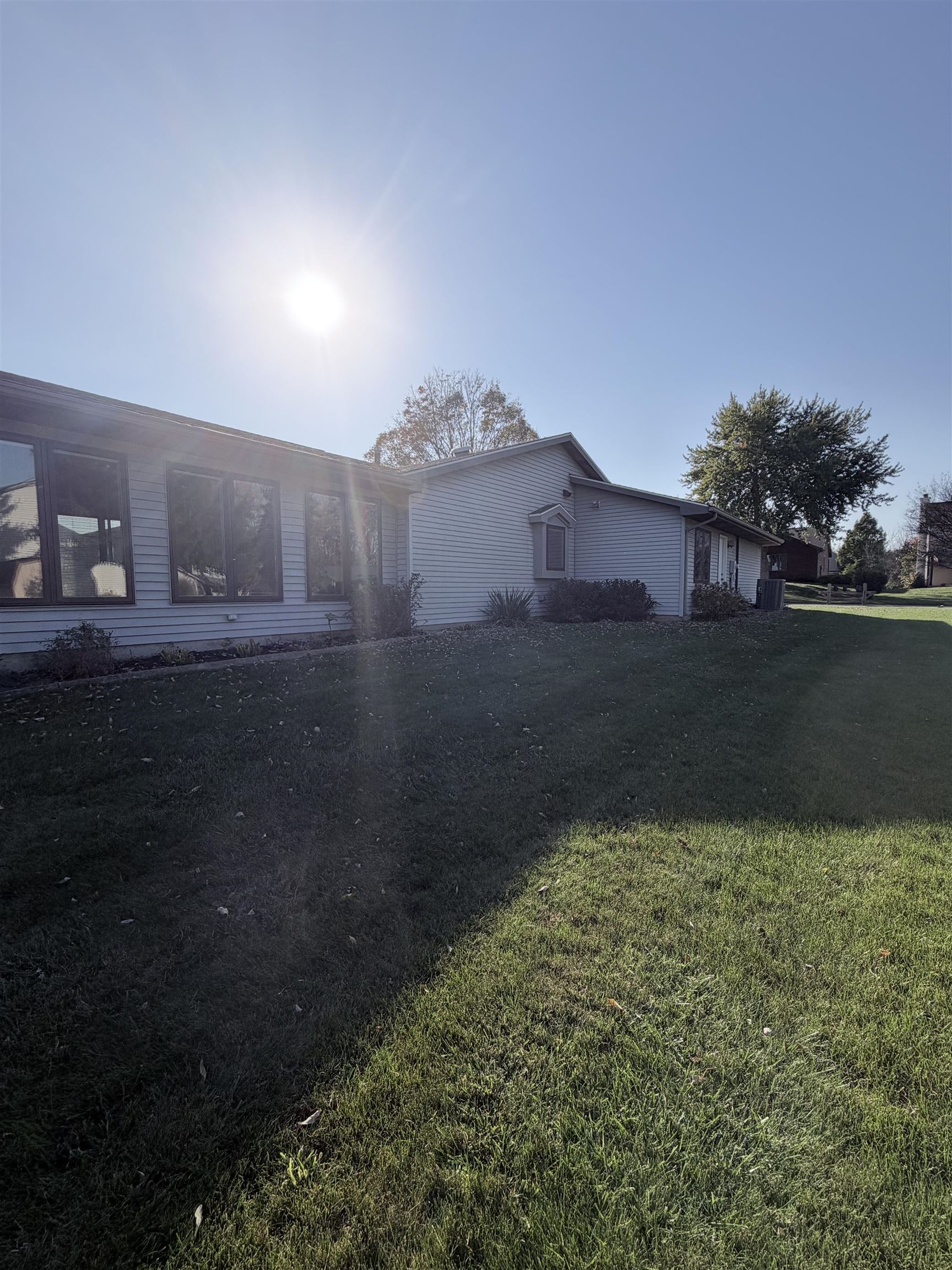 Exterior featuring light-toned horizontal siding, large multi-pane windows, a bay window, and a spacious lawn with mature trees