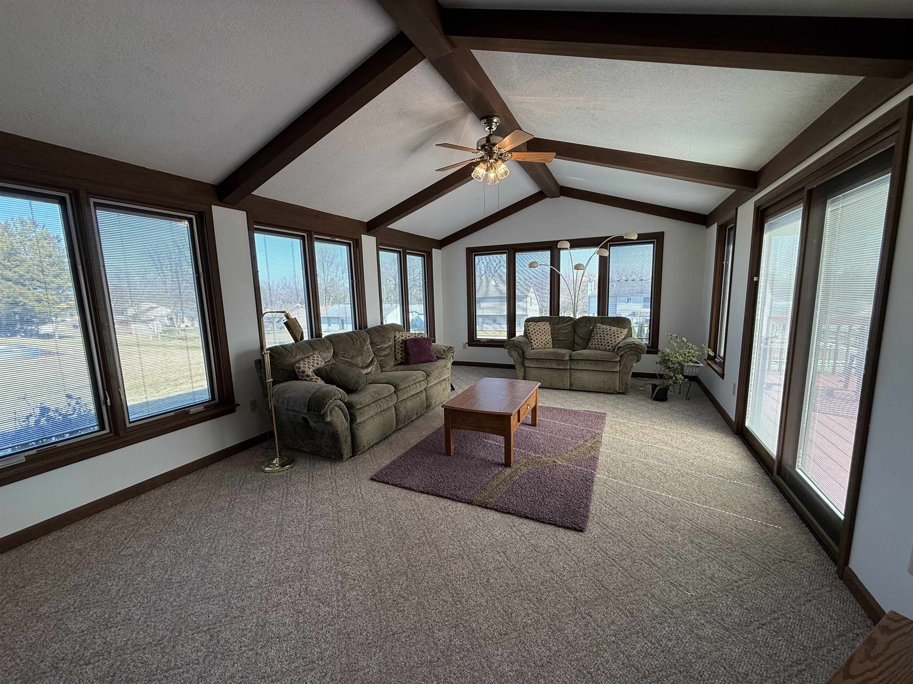 Living area featuring carpet floors, ceiling fan, beamed ceiling, and a textured ceiling