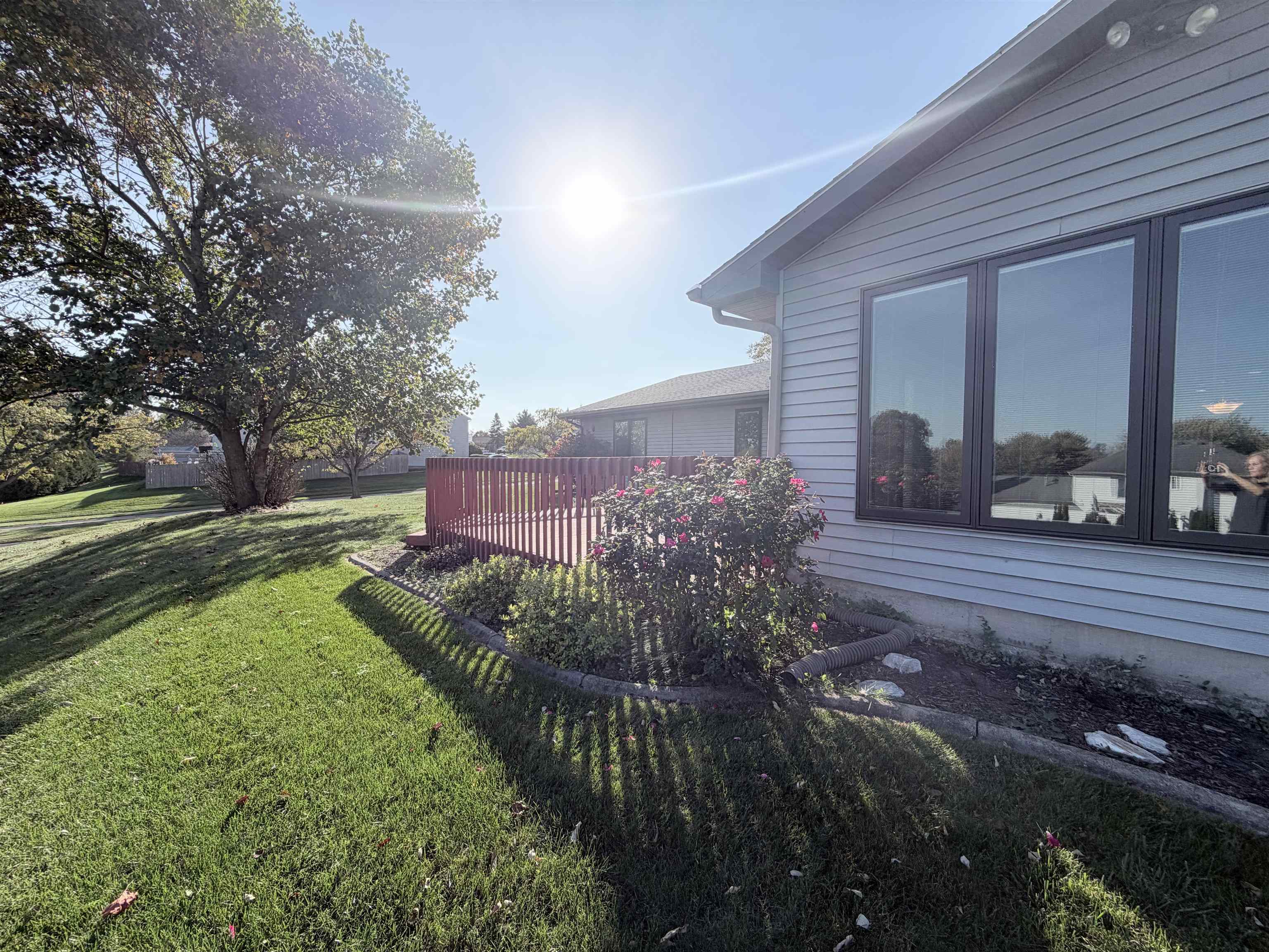 Exterior featuring horizontal lap siding, a raised wooden deck with railings, large picture windows with dark frames, and mature landscaping