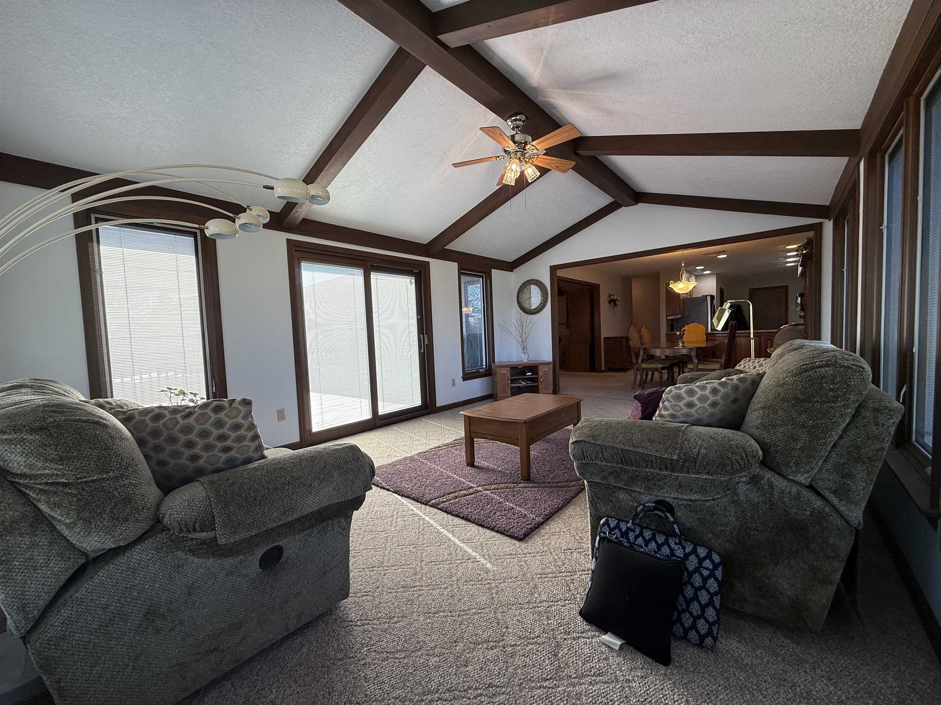Living area featuring light carpet, a textured ceiling, ceiling fan, and beamed ceiling