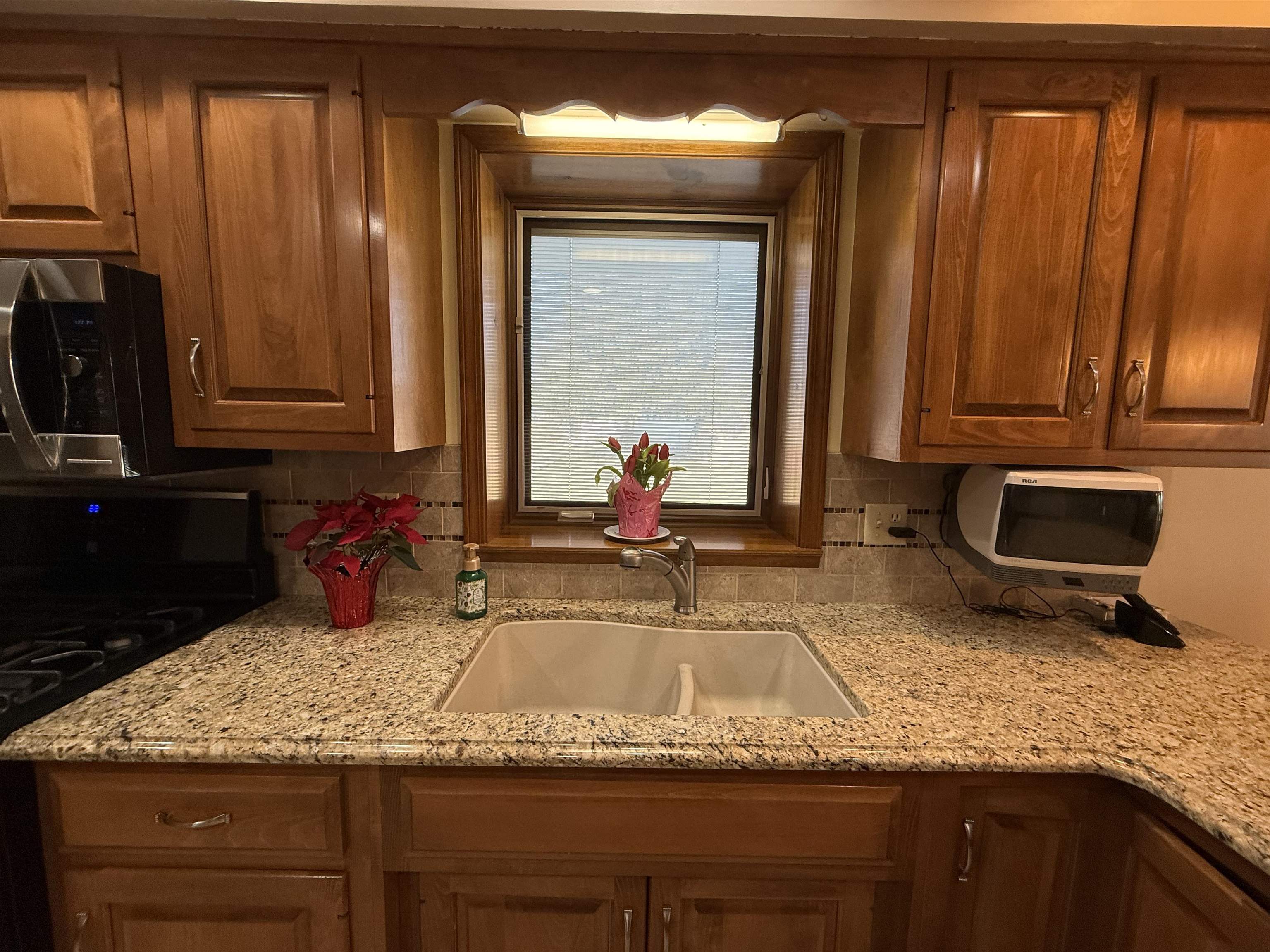 Kitchen with black range oven, light stone counters, wood finish cabinets, and stainless steel microwave