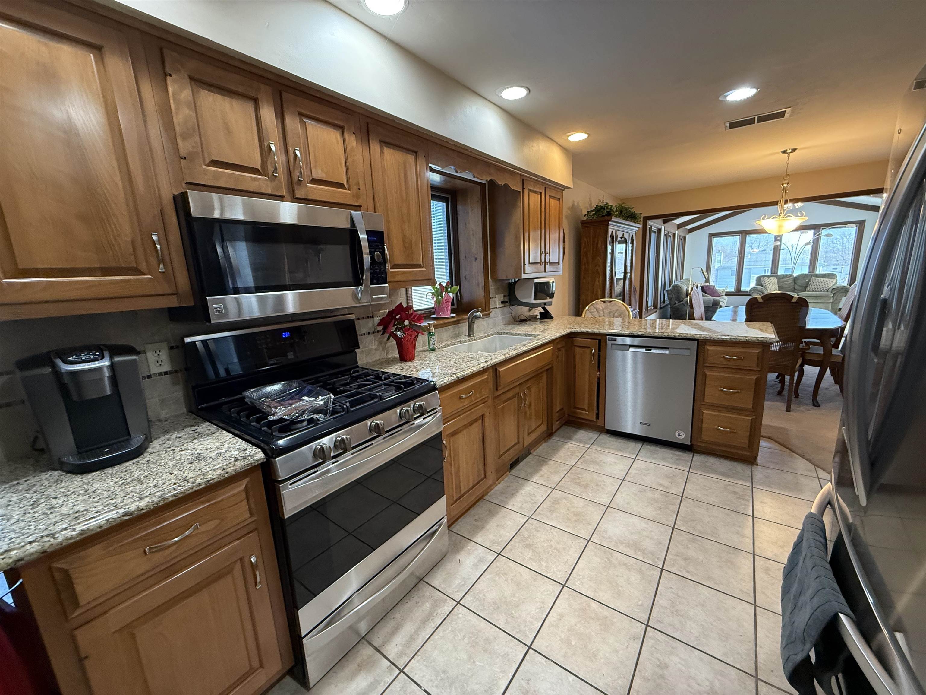 Kitchen featuring stainless steel appliances, light stone counters, a peninsula, and wood finish cabinets