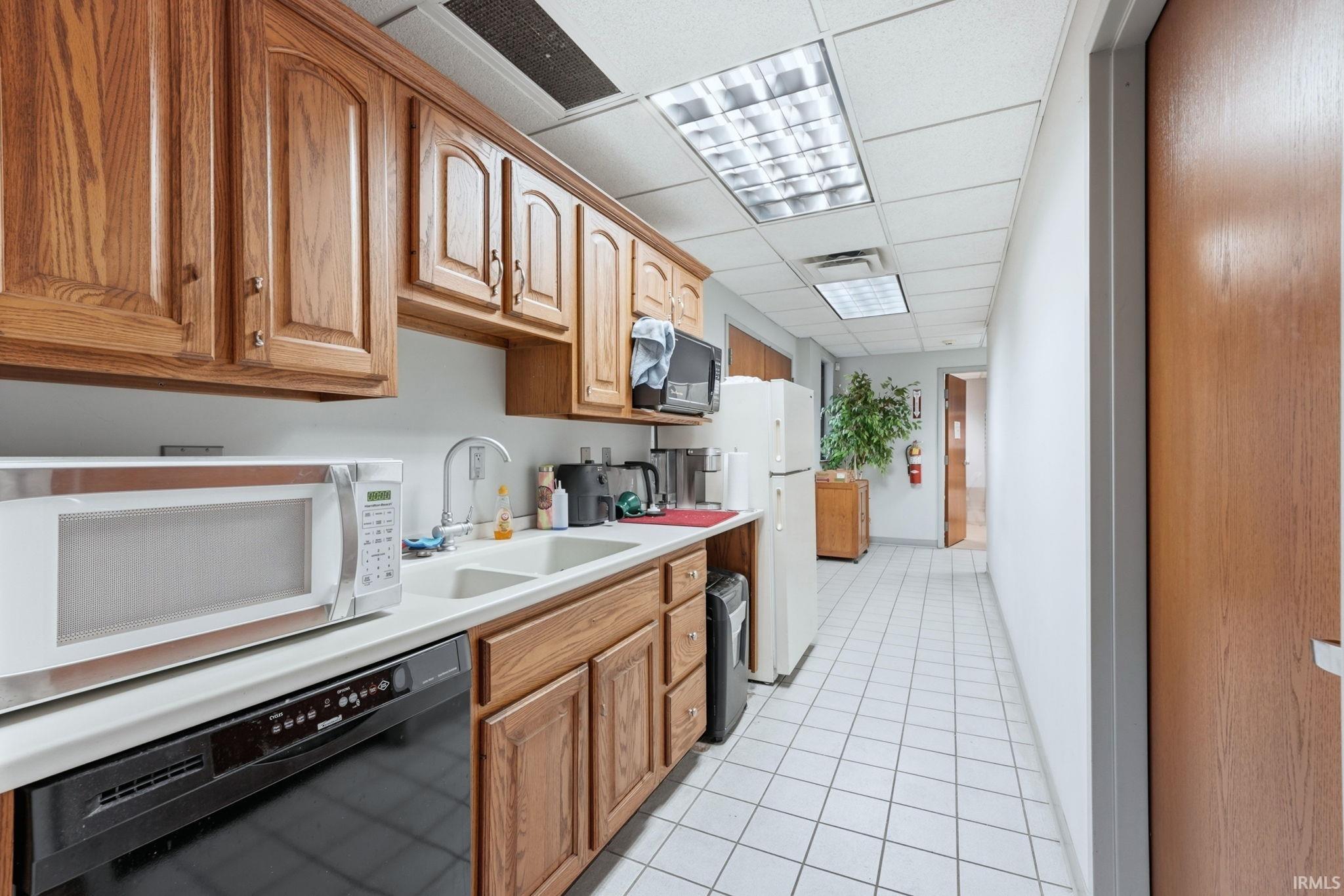 Kitchen with black appliances, a drop ceiling, light countertops, and wood finish cabinetry