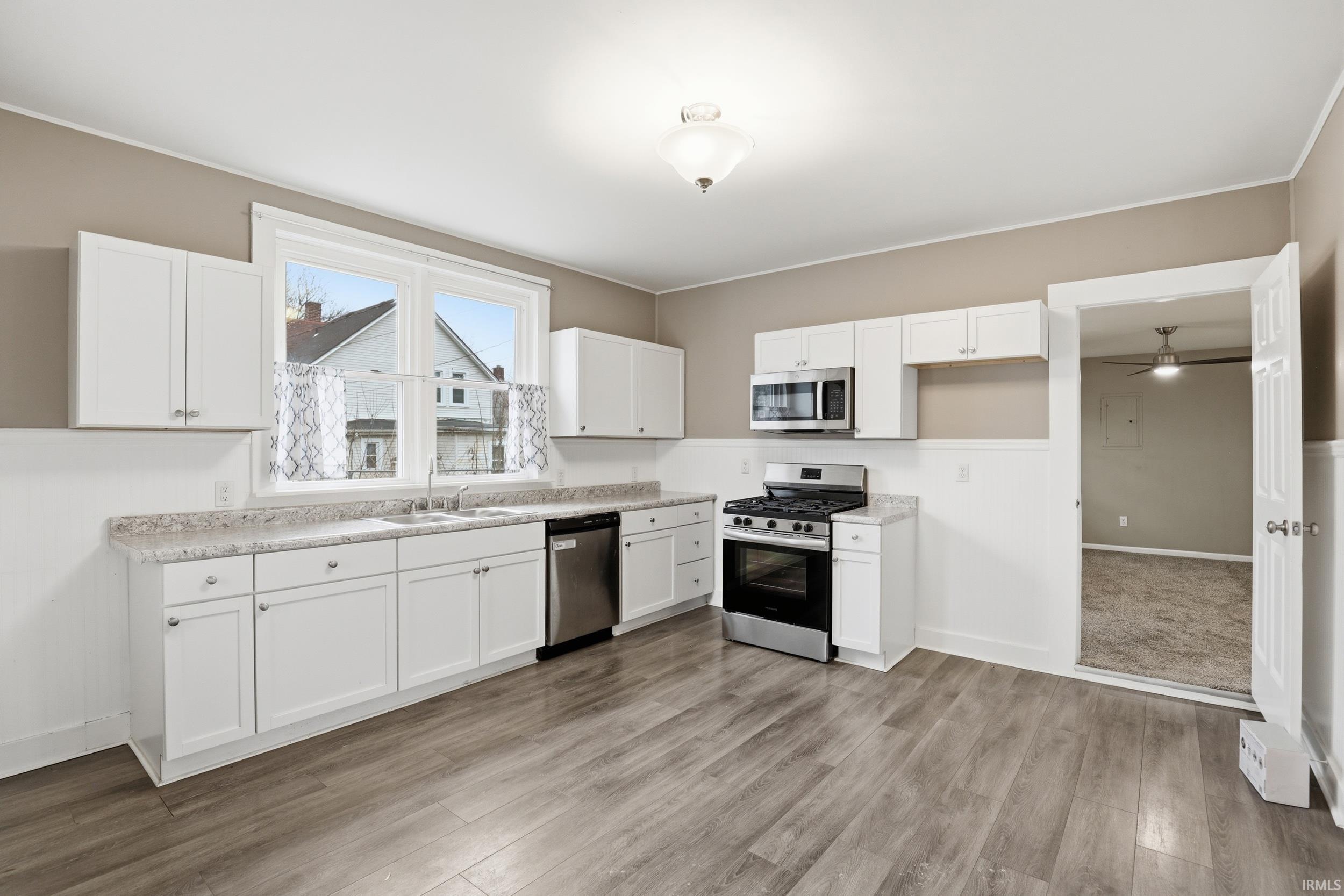 Kitchen with stainless steel appliances, light countertops, white cabinets, light wood finished floors, and ceiling fan