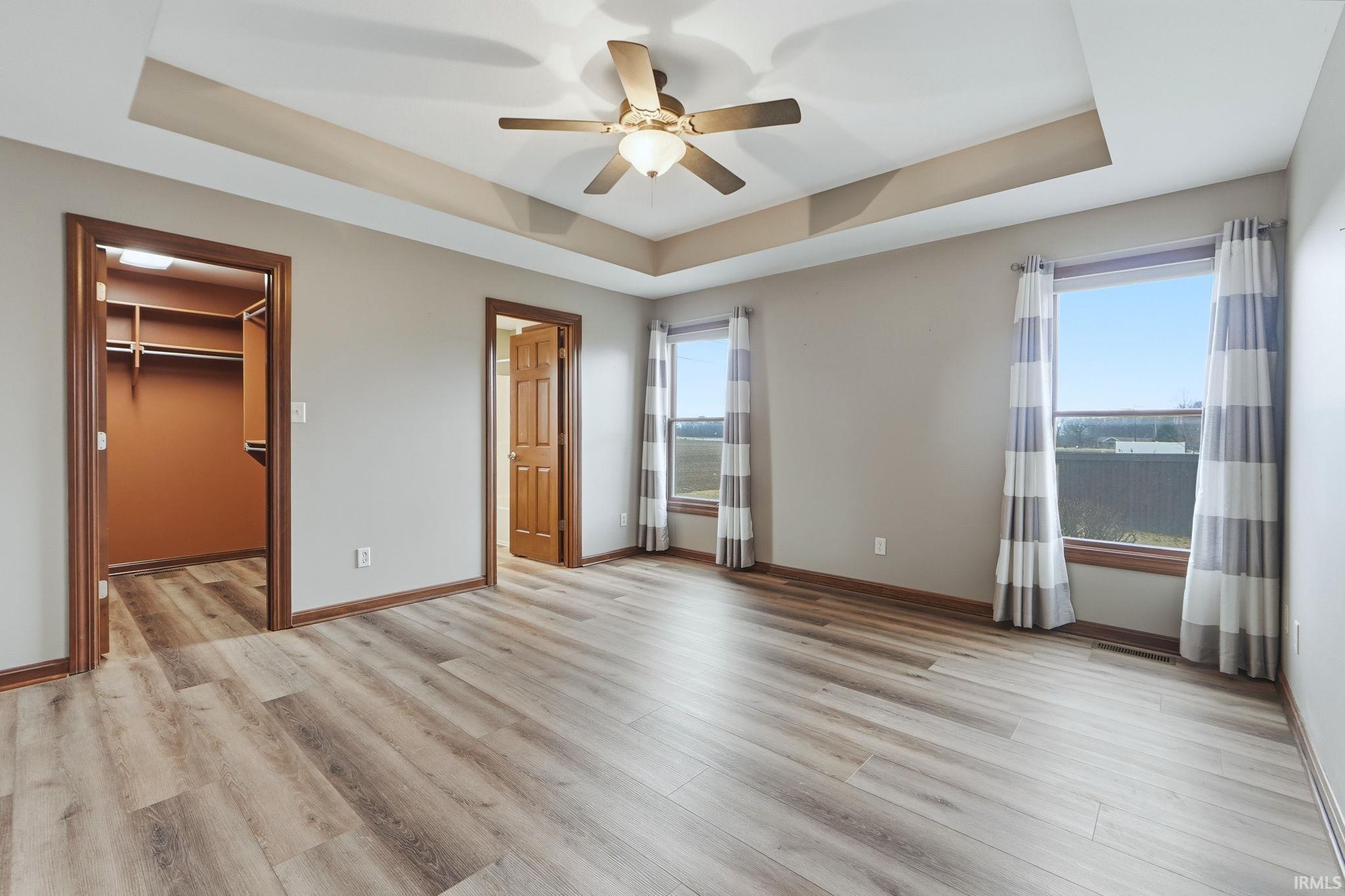 Unfurnished bedroom featuring a tray ceiling, a spacious closet, light wood-style flooring, and multiple windows