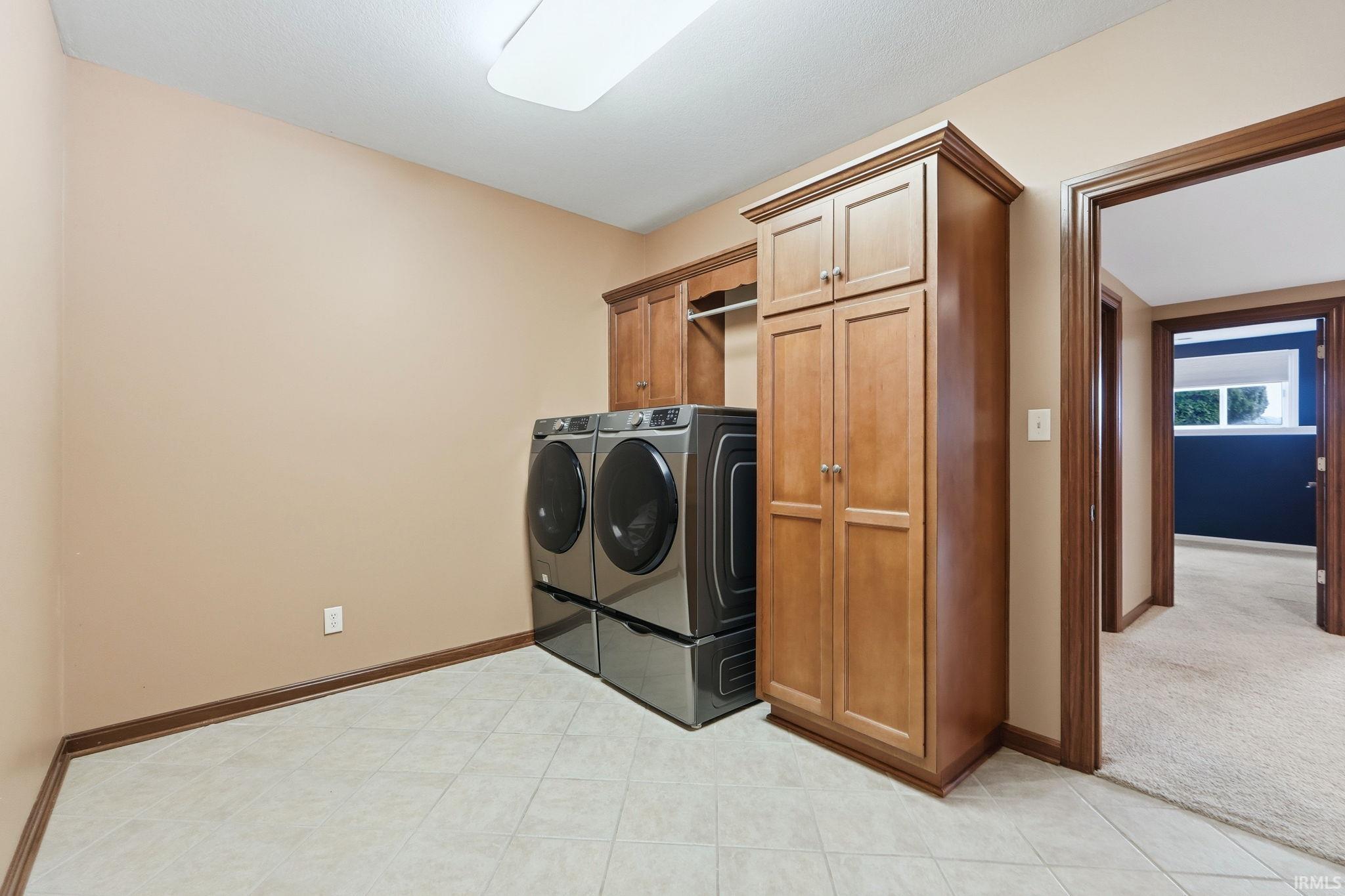 Laundry room featuring cabinet space, washer and clothes dryer, light tile patterned floors, and light colored carpet