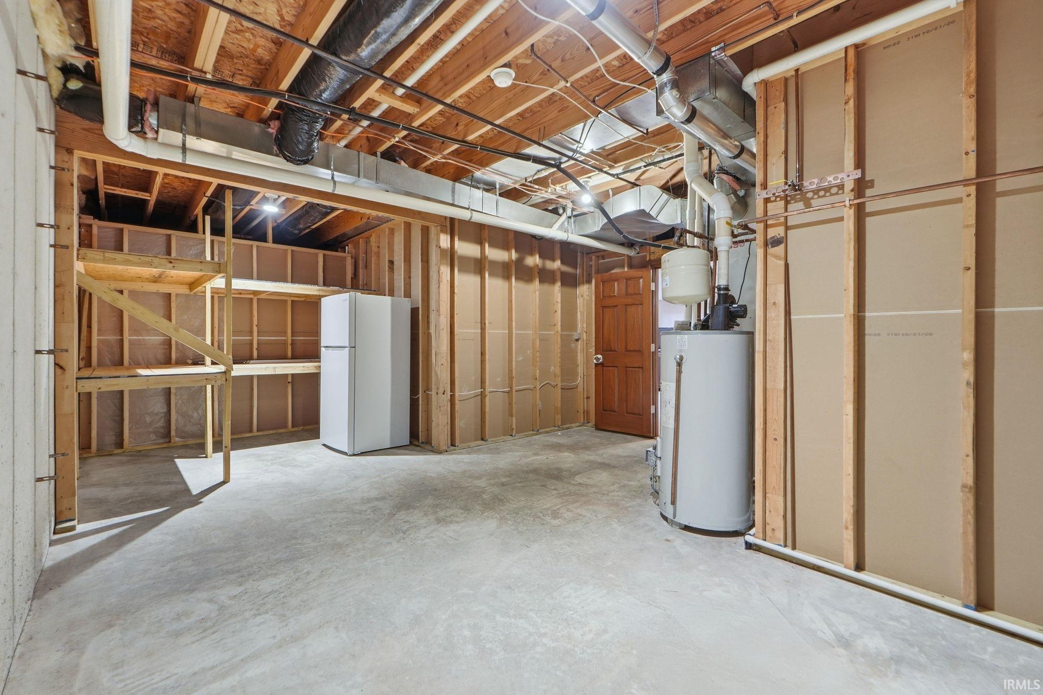 Unfinished basement with freestanding refrigerator and gas water heater