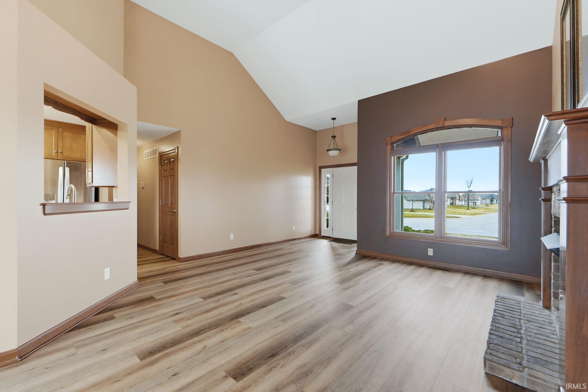 Unfurnished living room featuring lofted ceiling, light wood finished floors, a brick fireplace, and a water view