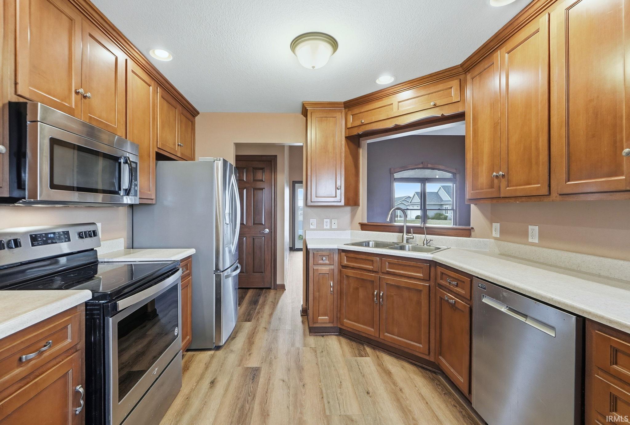 Kitchen featuring stainless steel appliances, recessed lighting, wood finish cabinetry, light countertops, and light wood-type flooring