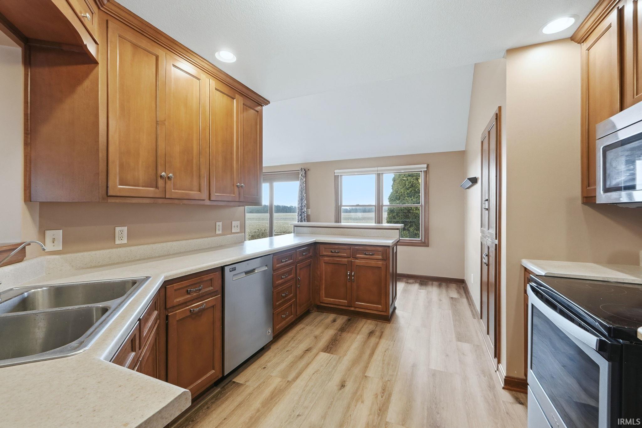 Kitchen with stainless steel appliances, light countertops, recessed lighting, light wood-style flooring, and a peninsula