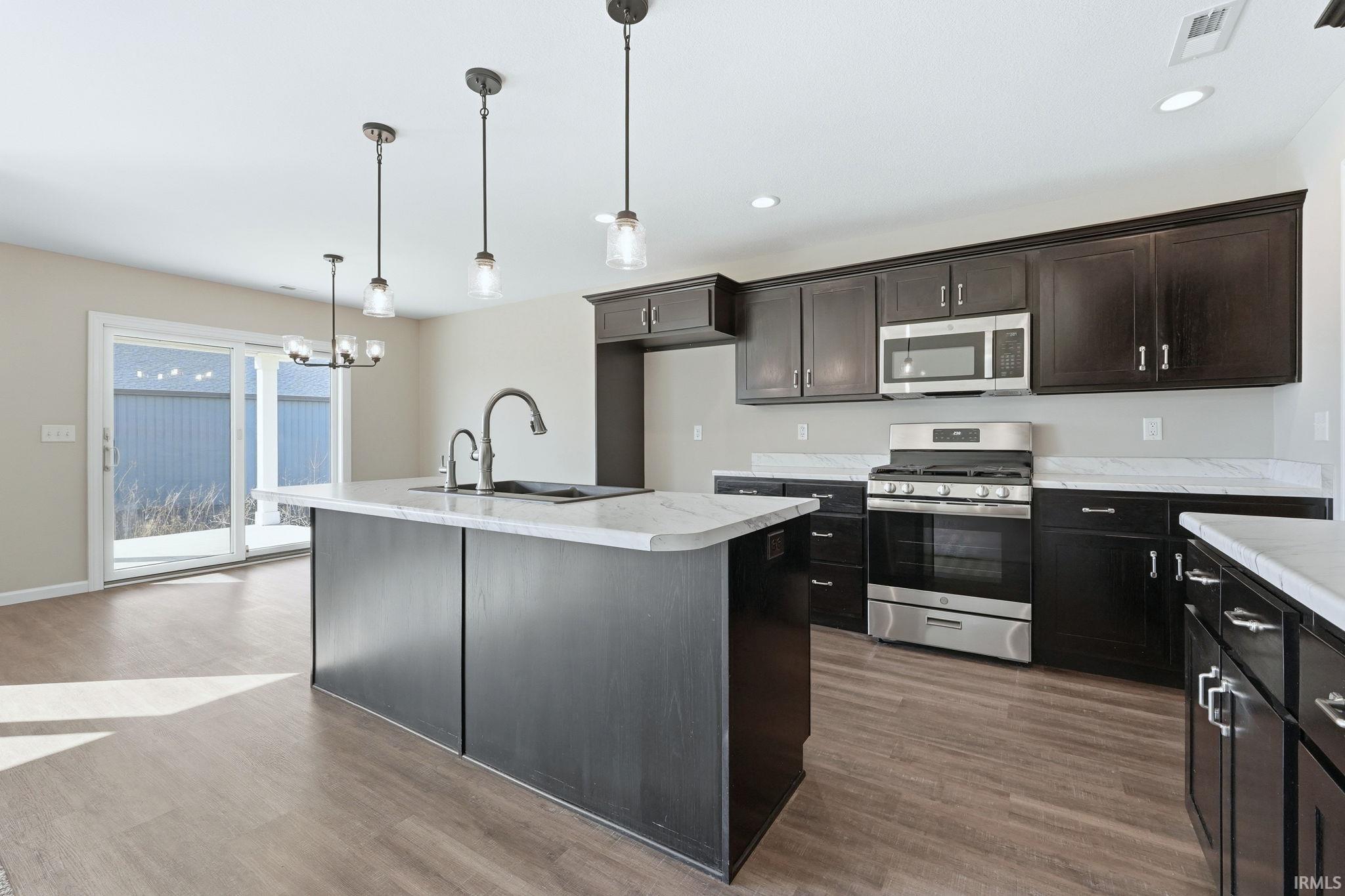 Kitchen featuring stainless steel appliances, light countertops, an island with sink, and dark wood-style floors