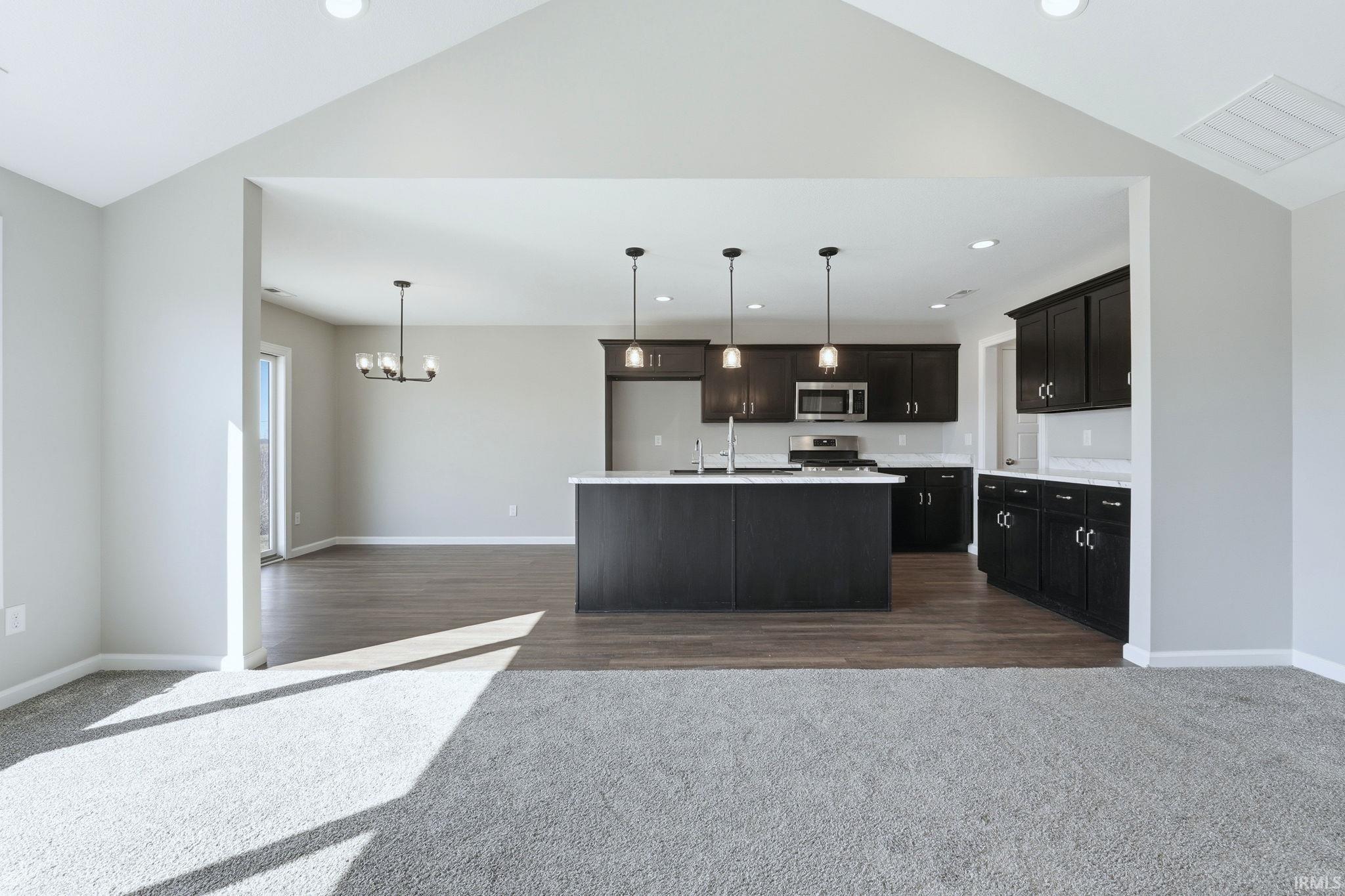 Kitchen with open floor plan, dark carpet, a center island with sink, stainless steel appliances, and lofted ceiling