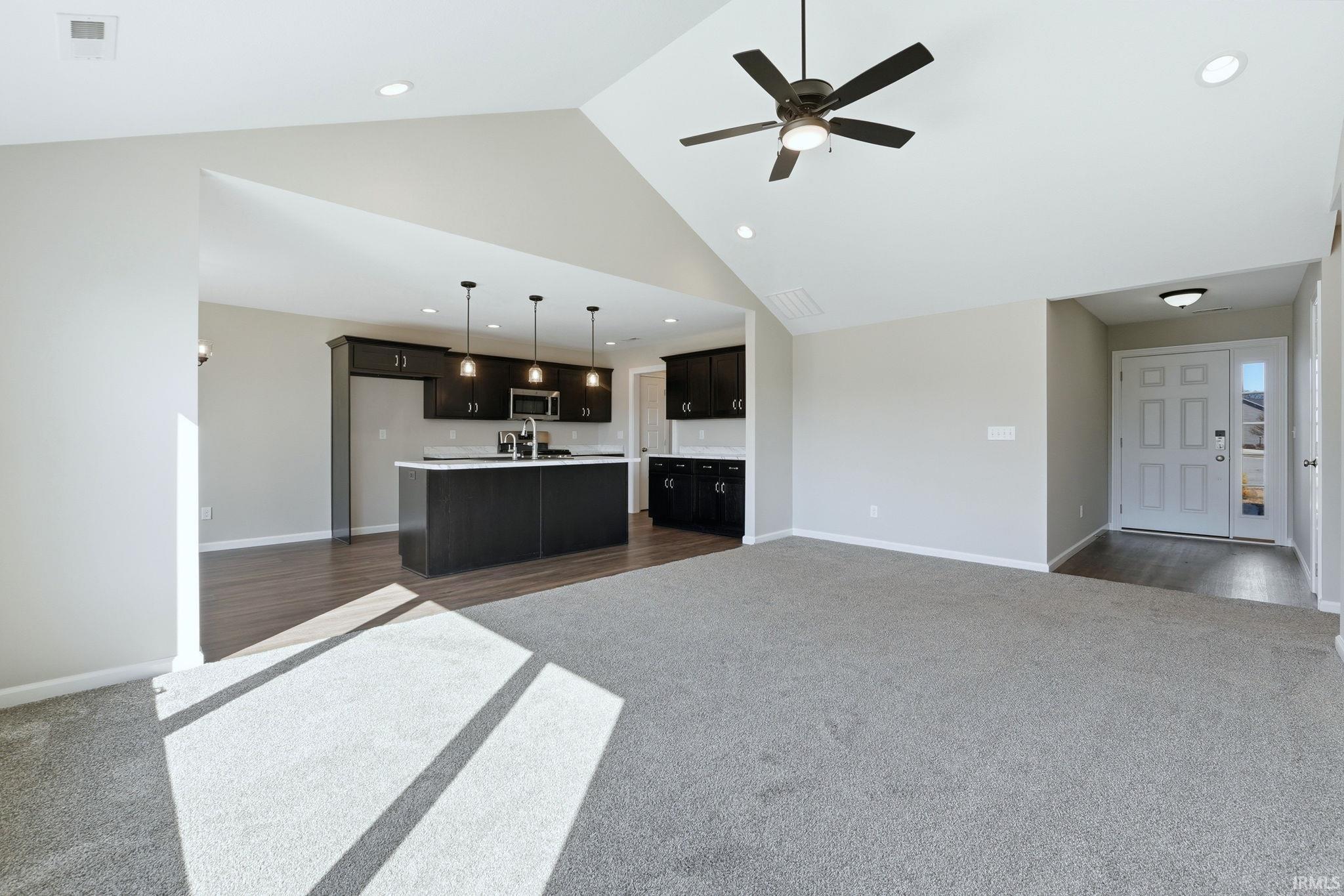 Unfurnished living room with dark carpet, ceiling fan, a high ceiling, and recessed lighting